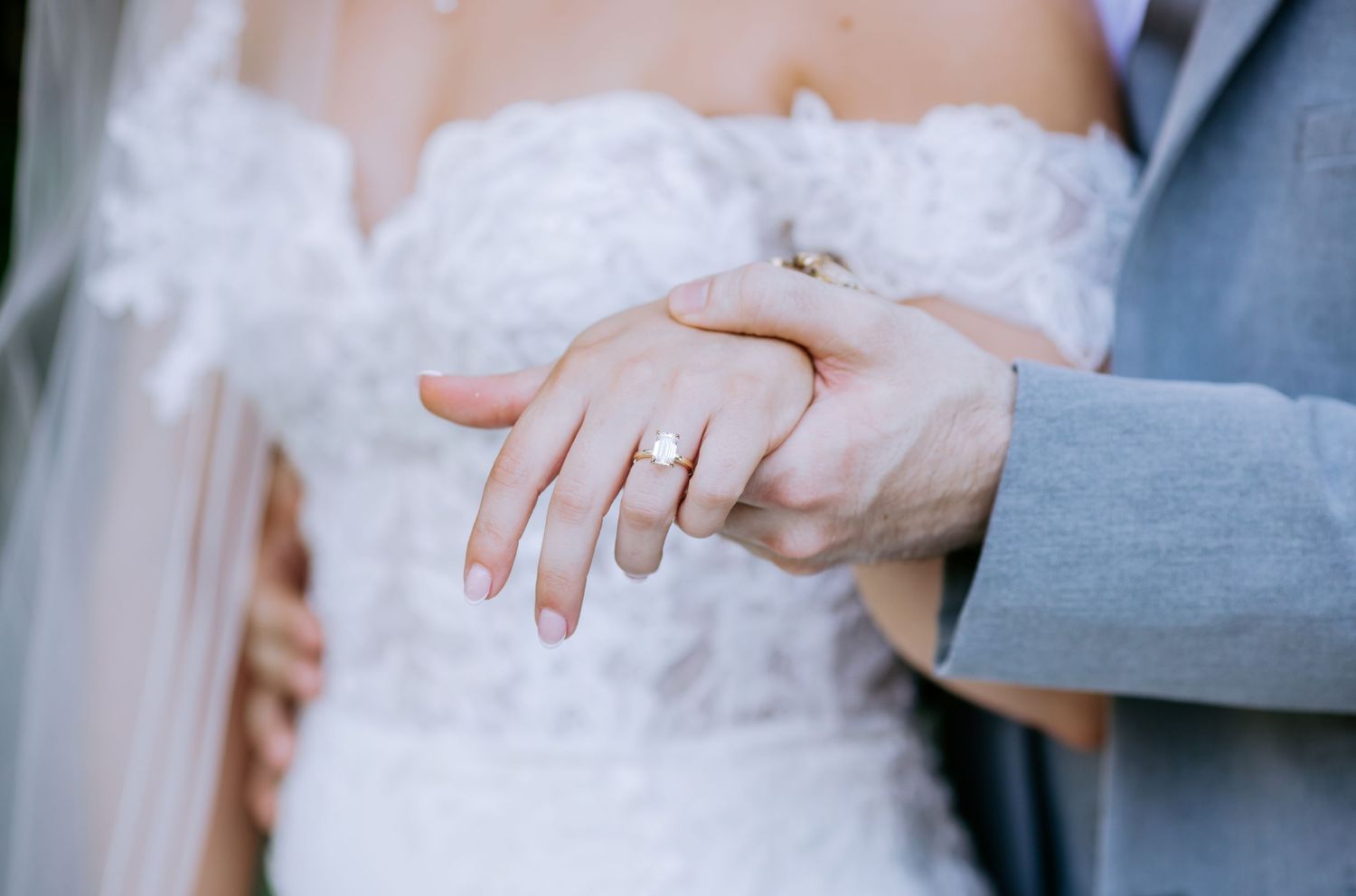 Close-up of newlyweds holding hands, showcasing a gold diamond engagement ring on the bride's finger at a wedding.