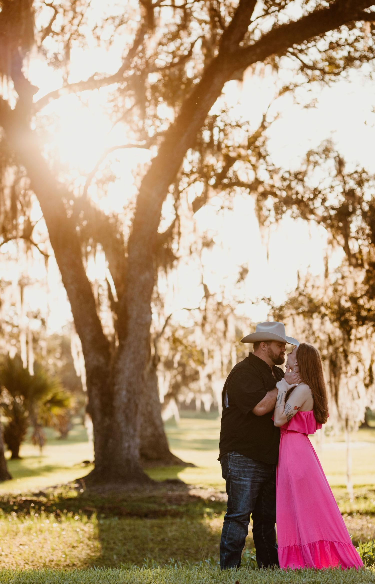 A couple shares a romantic moment at sunset among towering oak trees draped in Spanish moss.