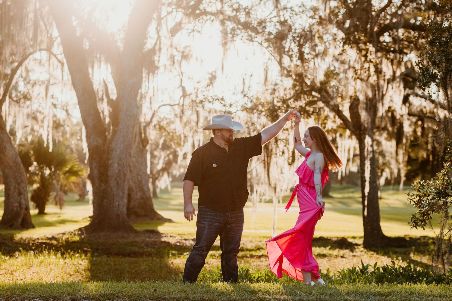 A couple in silhouette dances together in a sunlit park with tall trees creating a romantic atmosphere at sunset.