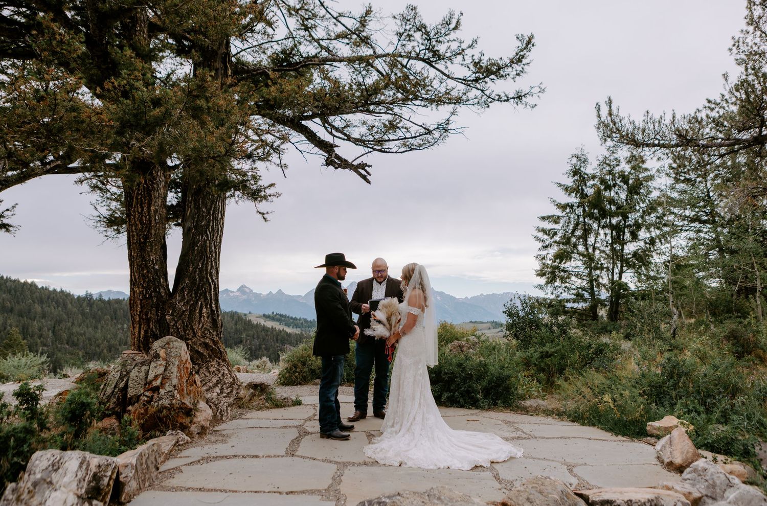 Couple exchanges vows at mountain overlook ceremony with stunning Rocky Mountain backdrop and rustic stone patio.
