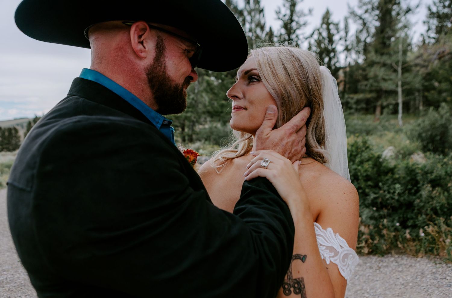 Groom in black cowboy hat tenderly holds bride's face during outdoor wedding ceremony.