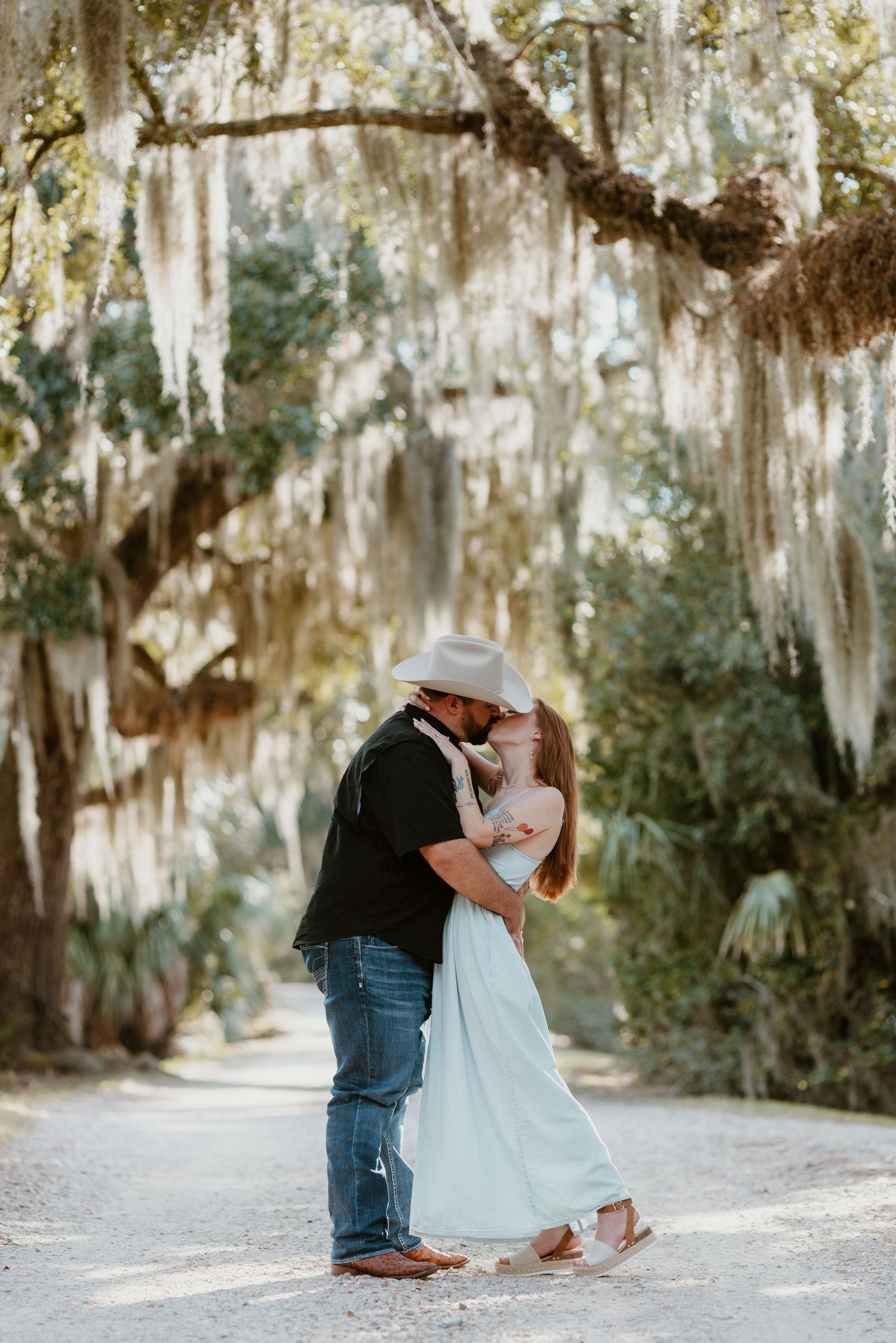 Romantic couple embraces under Spanish moss draped trees in a dreamy outdoor setting.