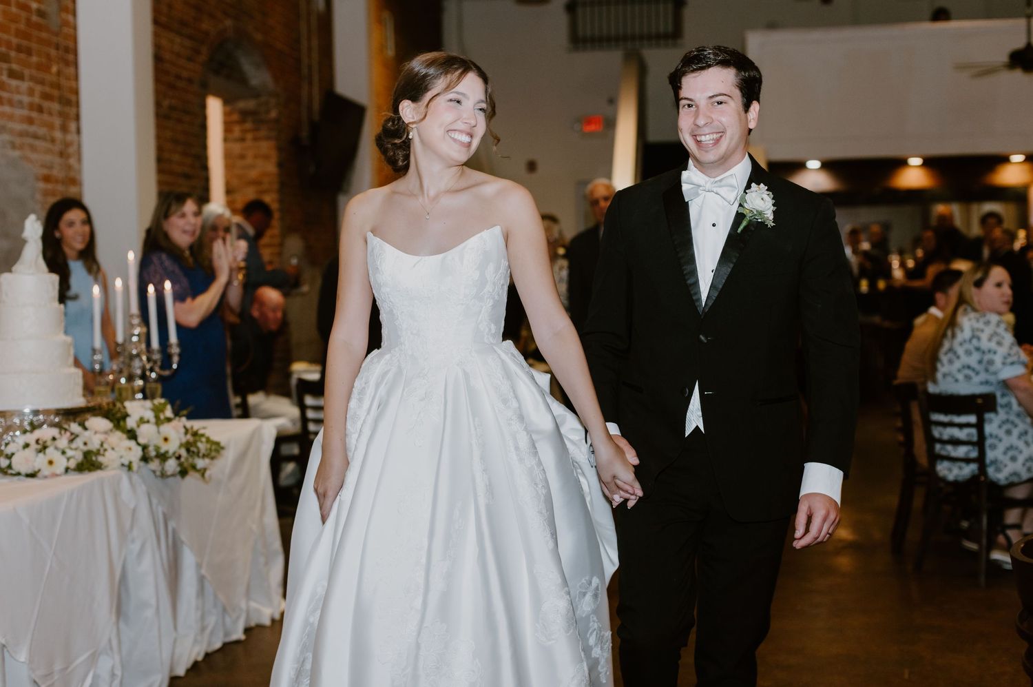 Bride and groom smile while holding hands during their wedding reception entrance in an elegant venue.