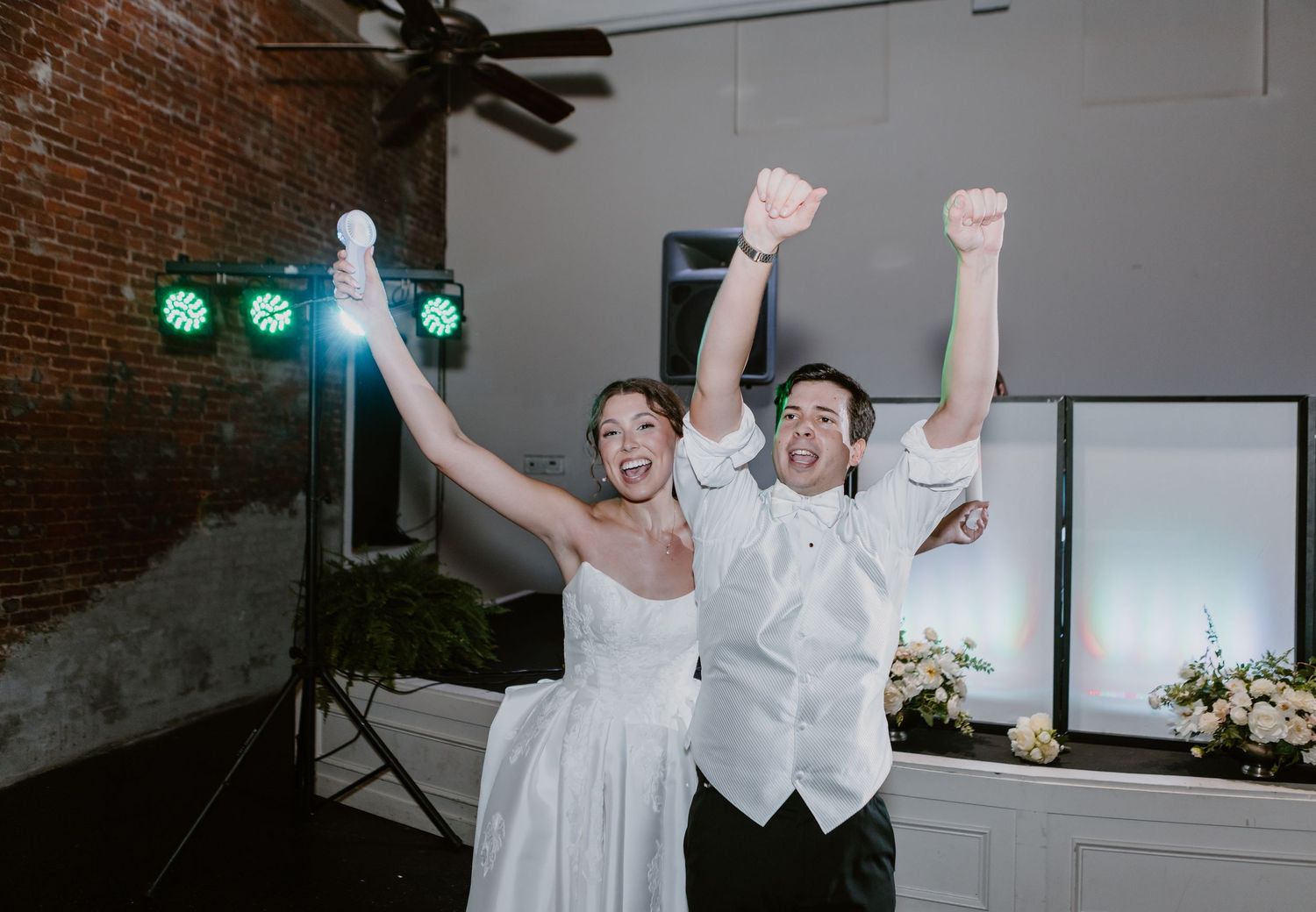 Excited bride and groom celebrating with arms raised at elegant wedding reception venue.