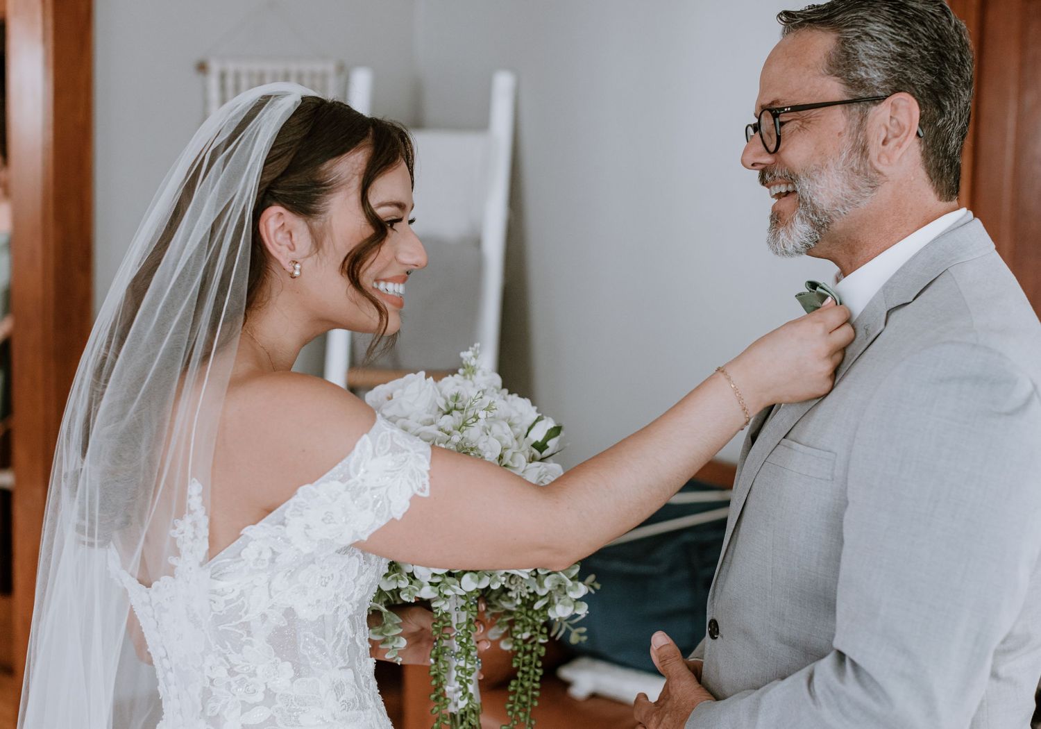 Bride in white lace gown adjusting groom's tie before wedding ceremony.