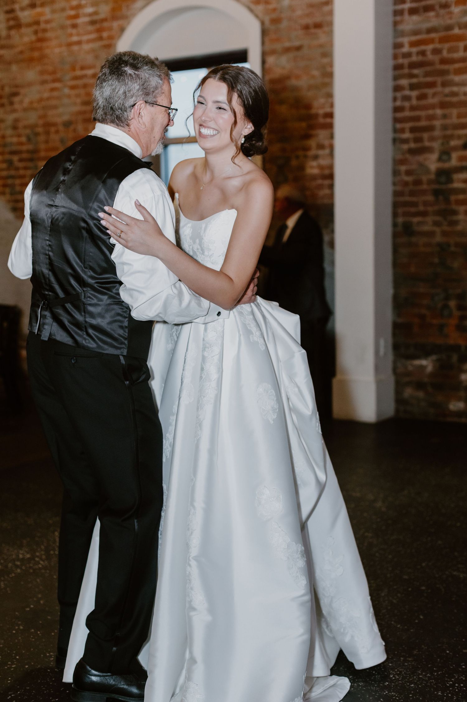 Bride in white strapless gown shares joyful father-daughter dance at elegant wedding reception.