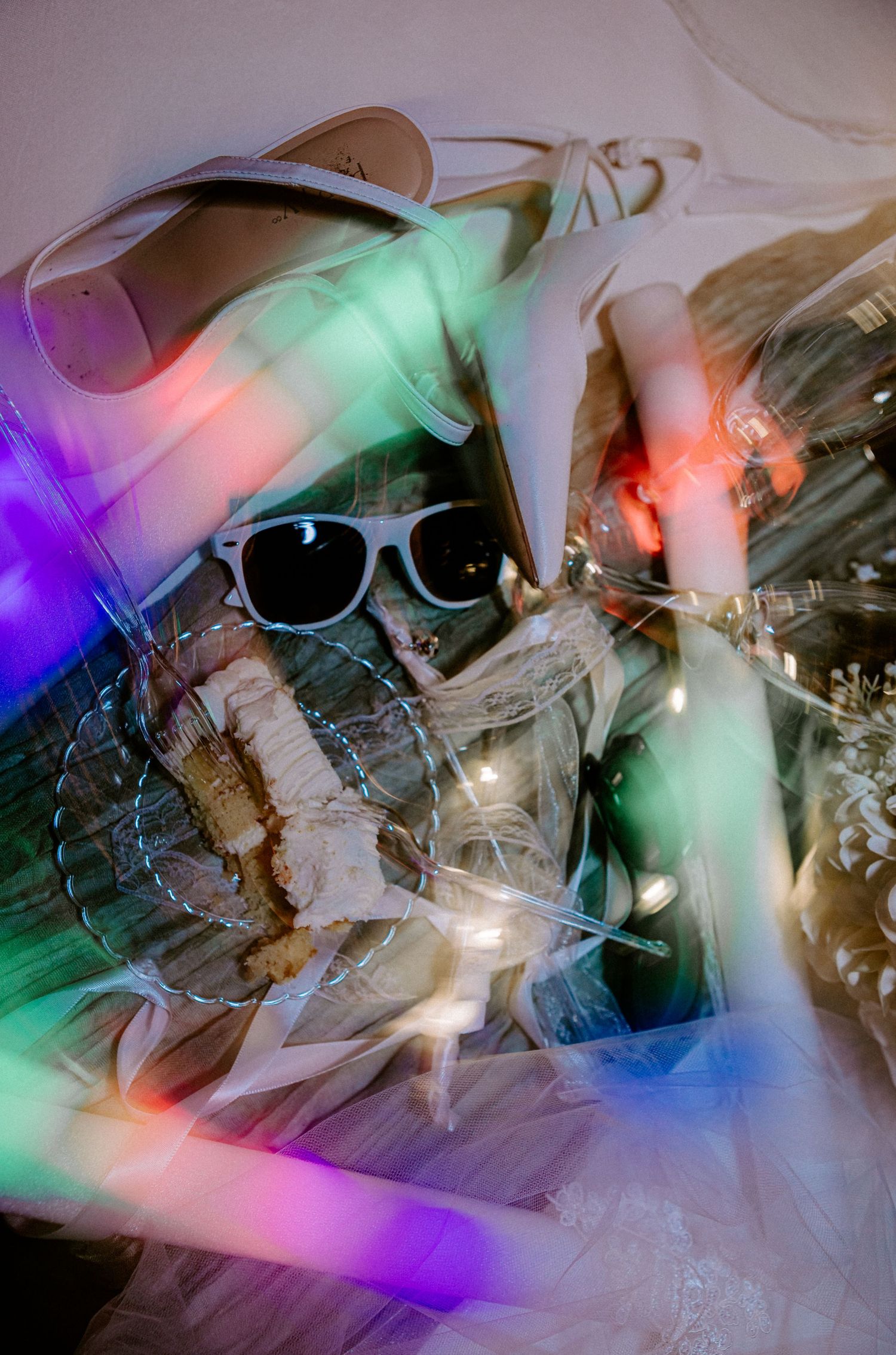 Colorful light streaks illuminate wedding accessories including heels, sunglasses, and glow sticks on a table.