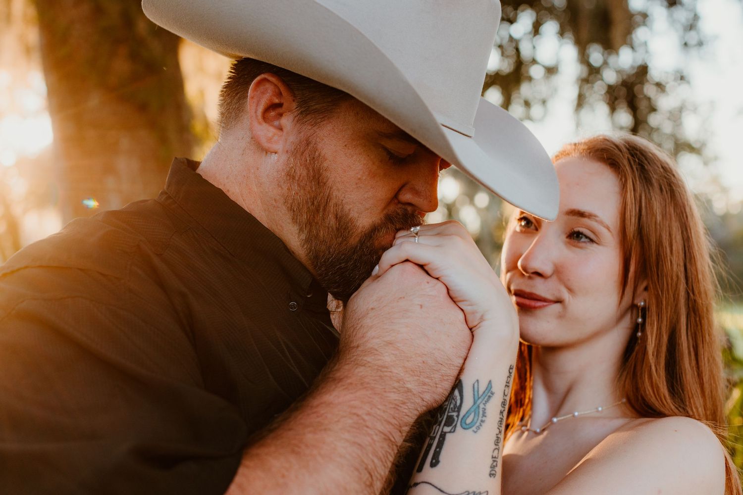 Romantic sunset engagement photos showing couple in cowboy hats sharing tender moments together.