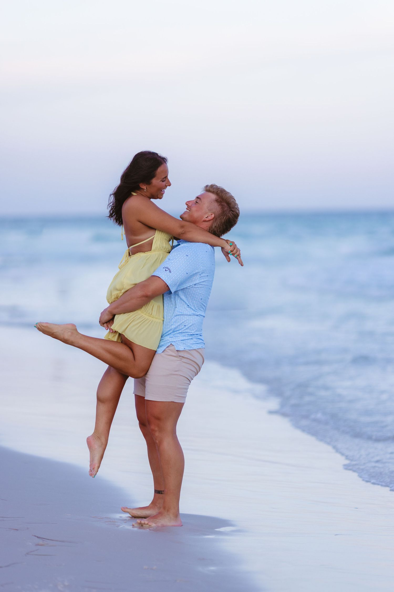 A romantic couple embraces and plays together on a misty beach at sunset.