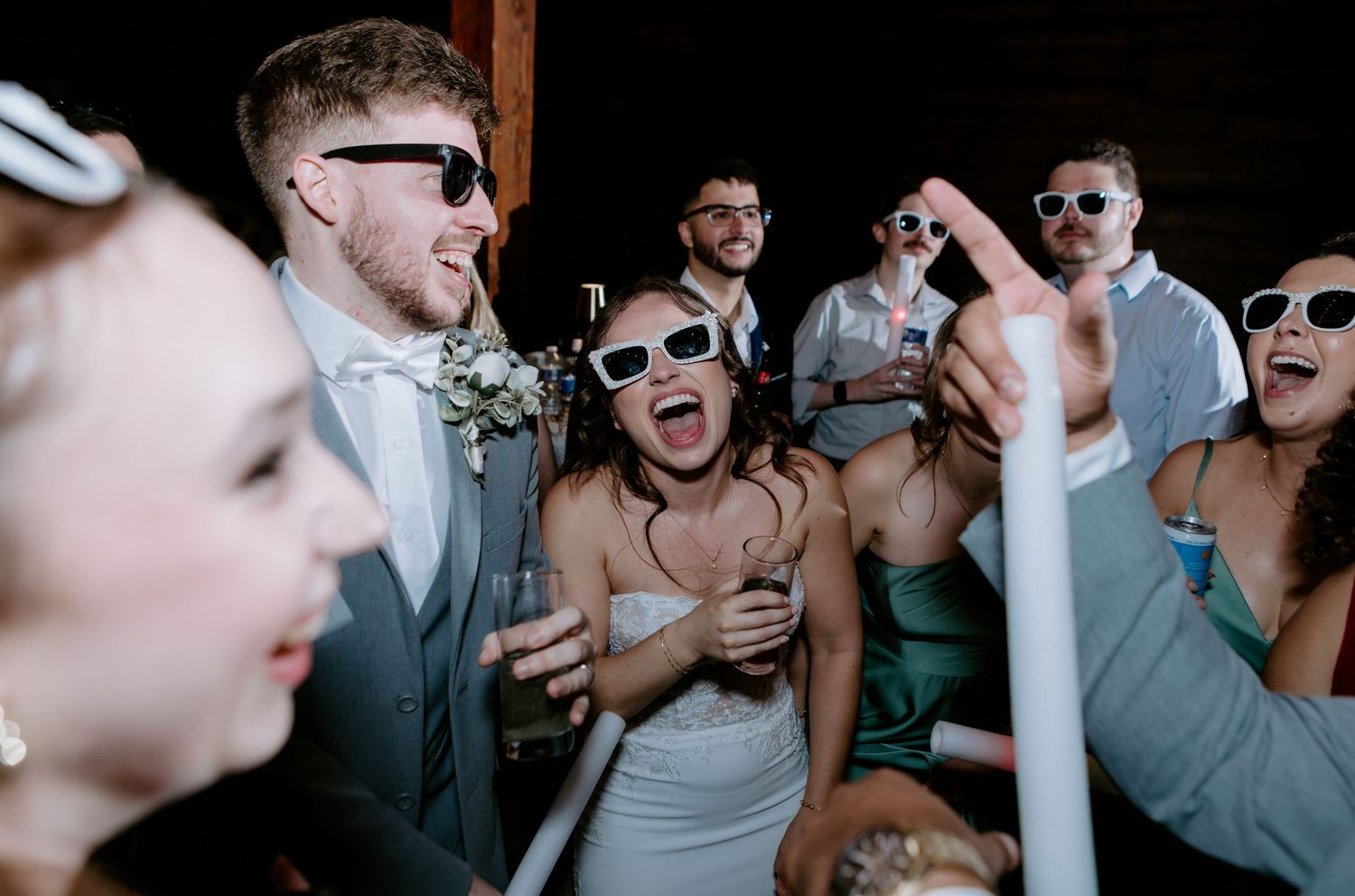 Bride and groom celebrating with guests wearing white sunglasses during lively wedding reception.