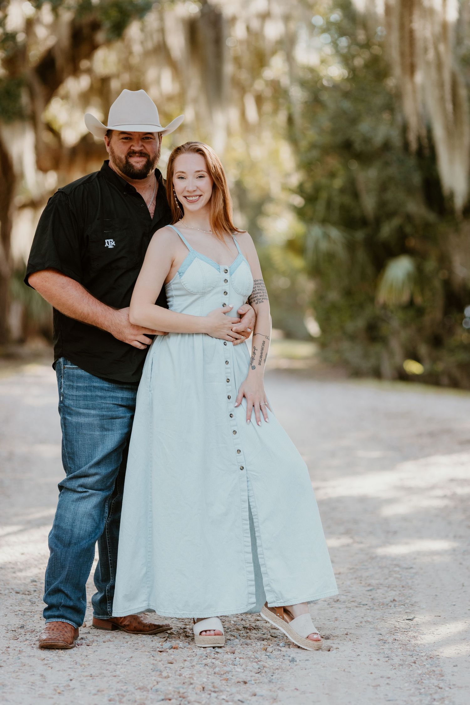 Couple shares tender moments while sitting together on a sunlit path beneath moss-covered trees.