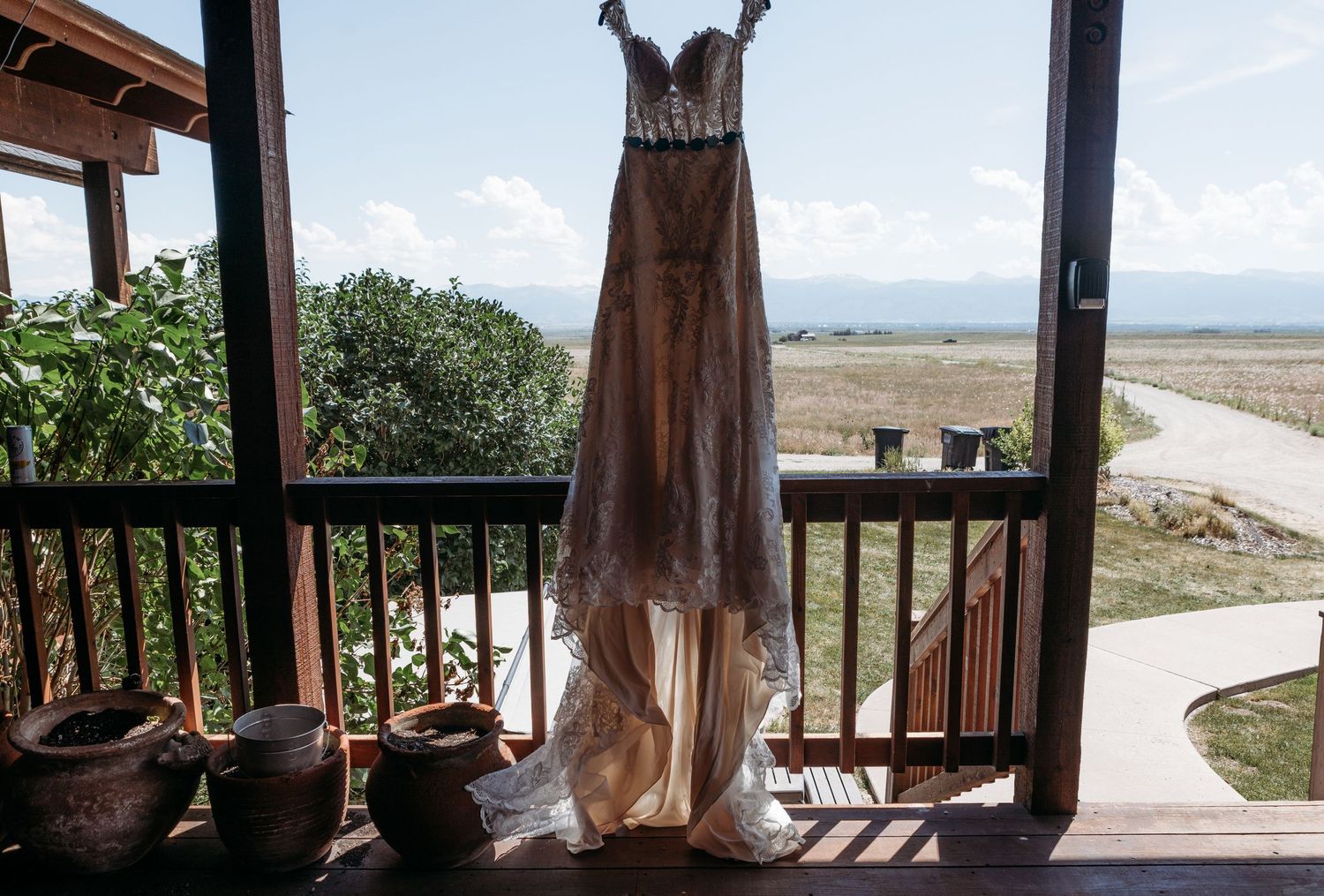 Wedding dress hanging on a rustic porch with scenic countryside views and mountains in the background.