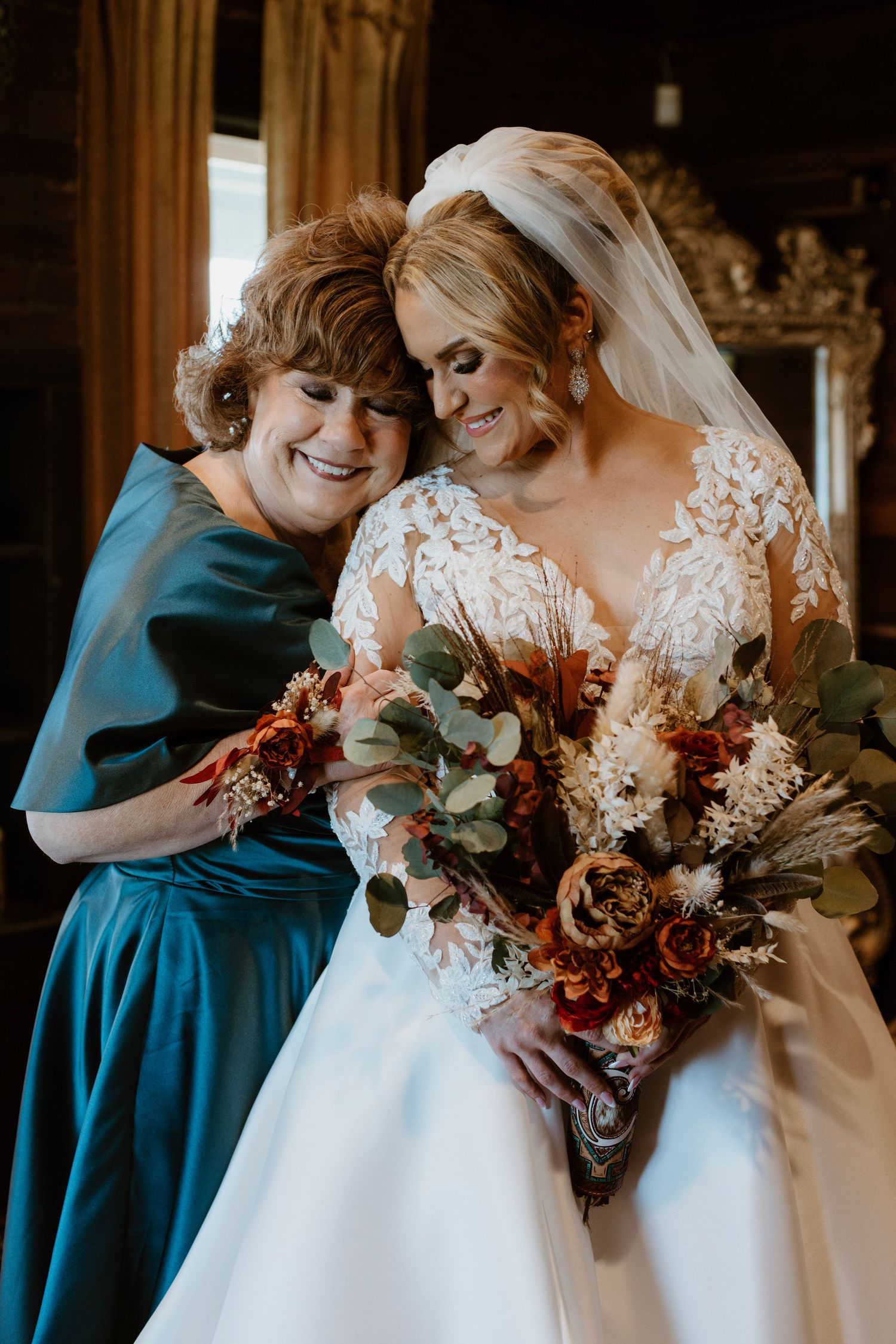 Bridesmaids in teal dresses share tender moments with bride in white lace gown holding autumn-colored bouquet.