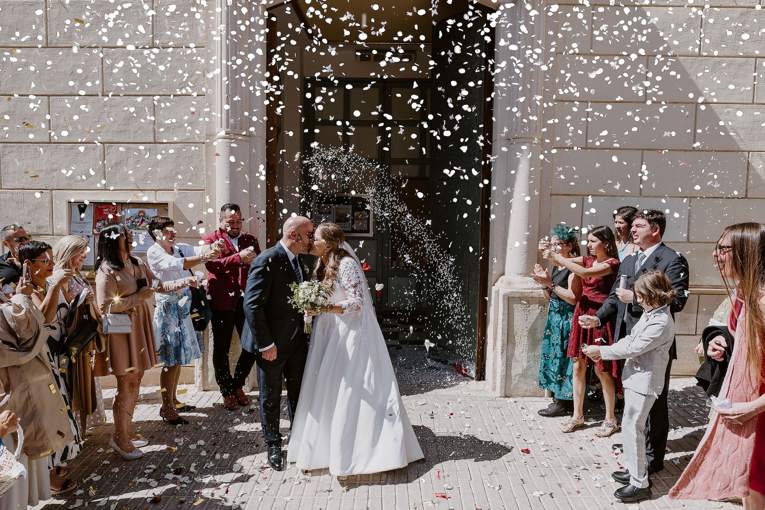 Newlyweds exit church while guests shower them with confetti in celebration.