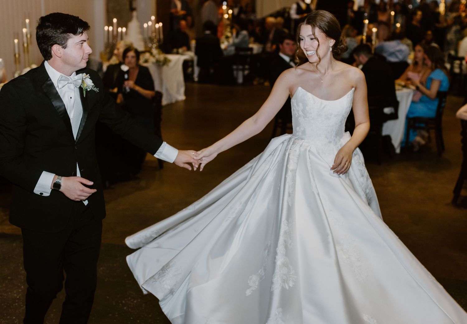Bride in white ballgown and groom in black tuxedo share first dance at elegant wedding reception.