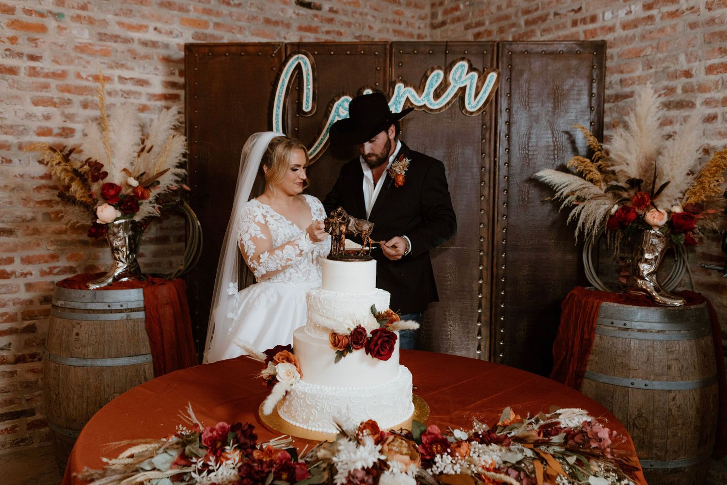 Newlyweds cut white wedding cake at rustic barn venue with floral decor.