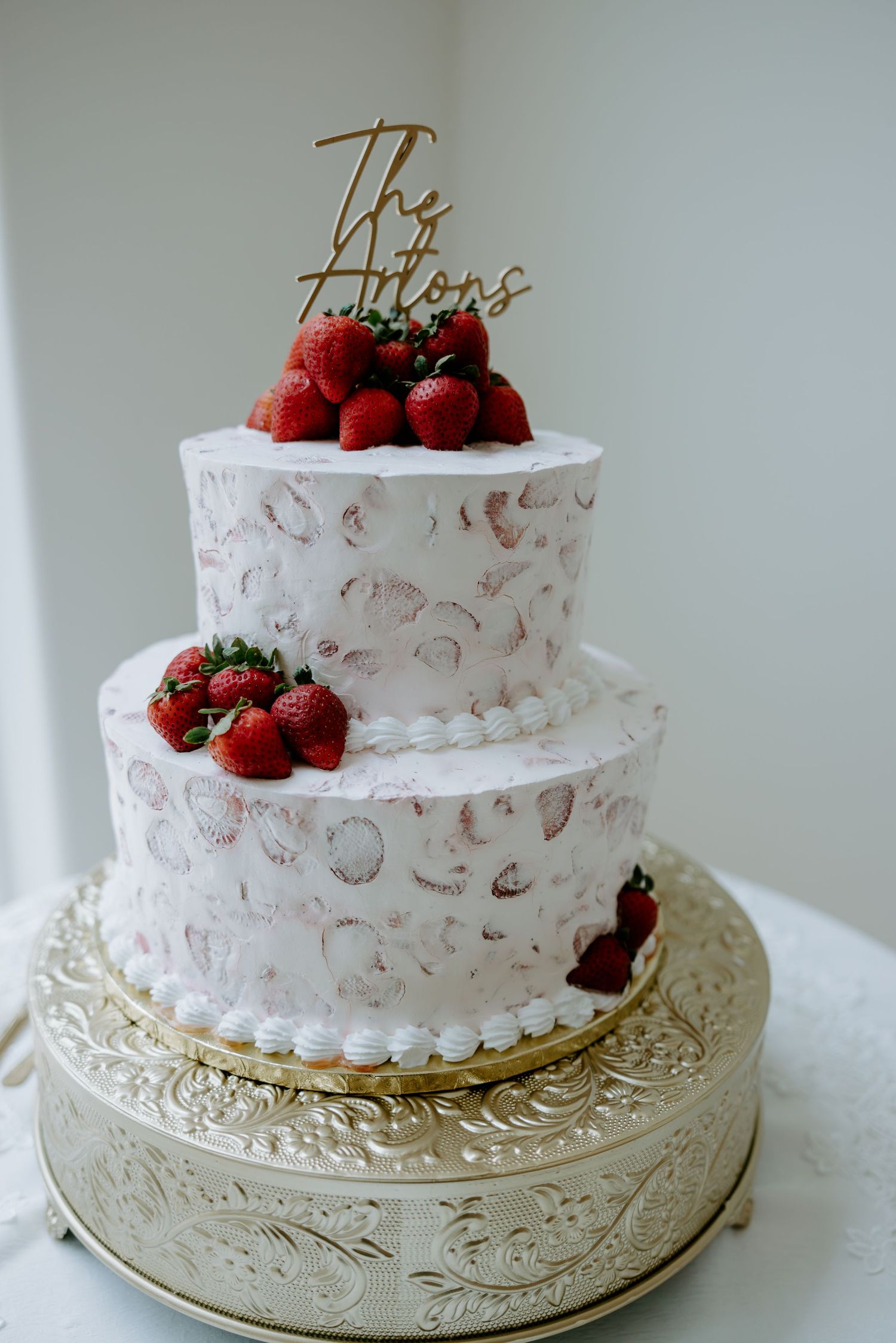 Two-tier white wedding cake with seashell designs, fresh strawberries and a gold 