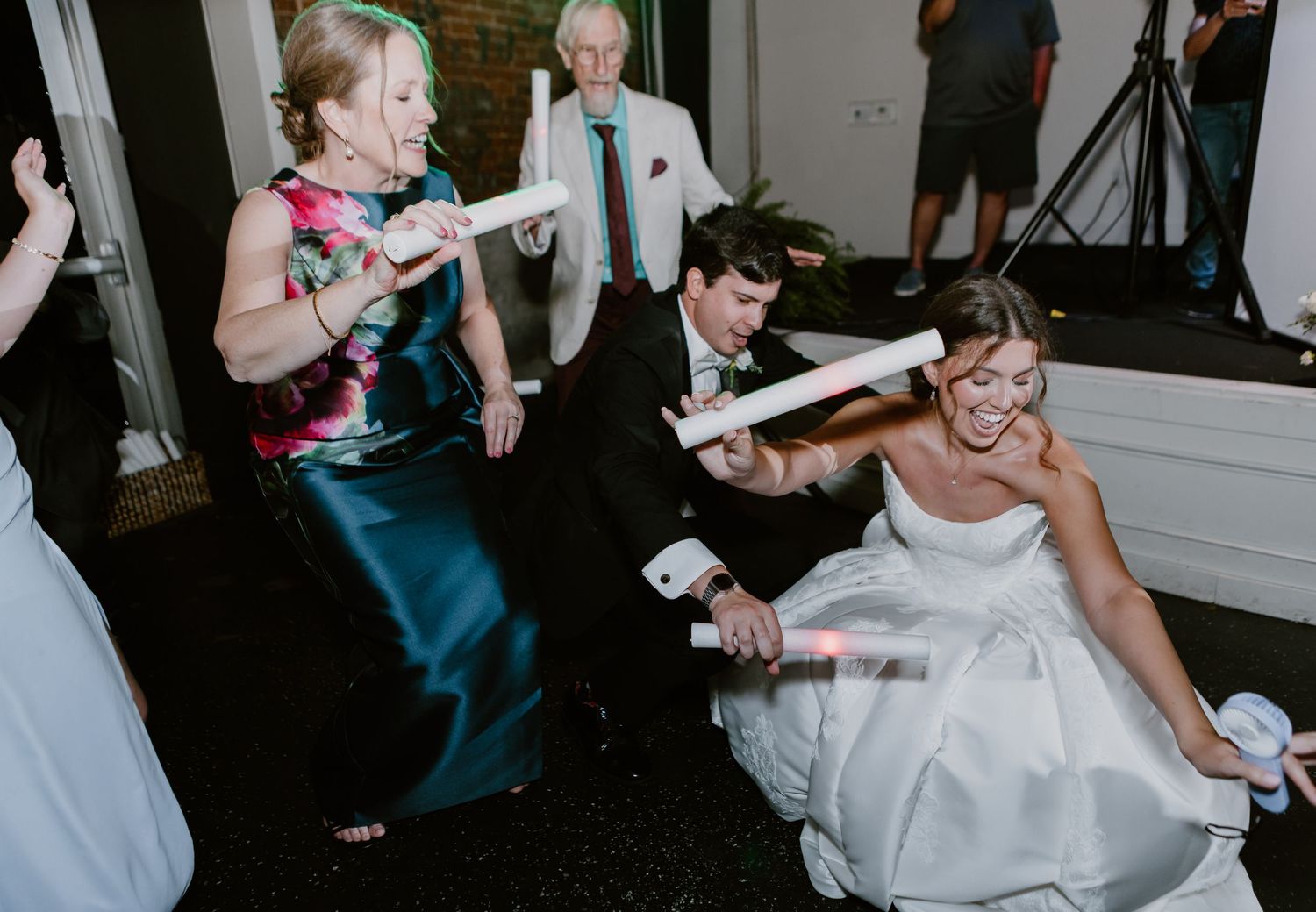 Bride dancing energetically with guests including an older woman in a floral dress at a wedding reception.