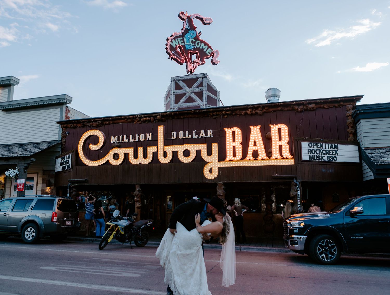 Neon-lit Million Dollar Cowboy Bar facade at dusk in Jackson Hole Wyoming with pedestrians outside.
