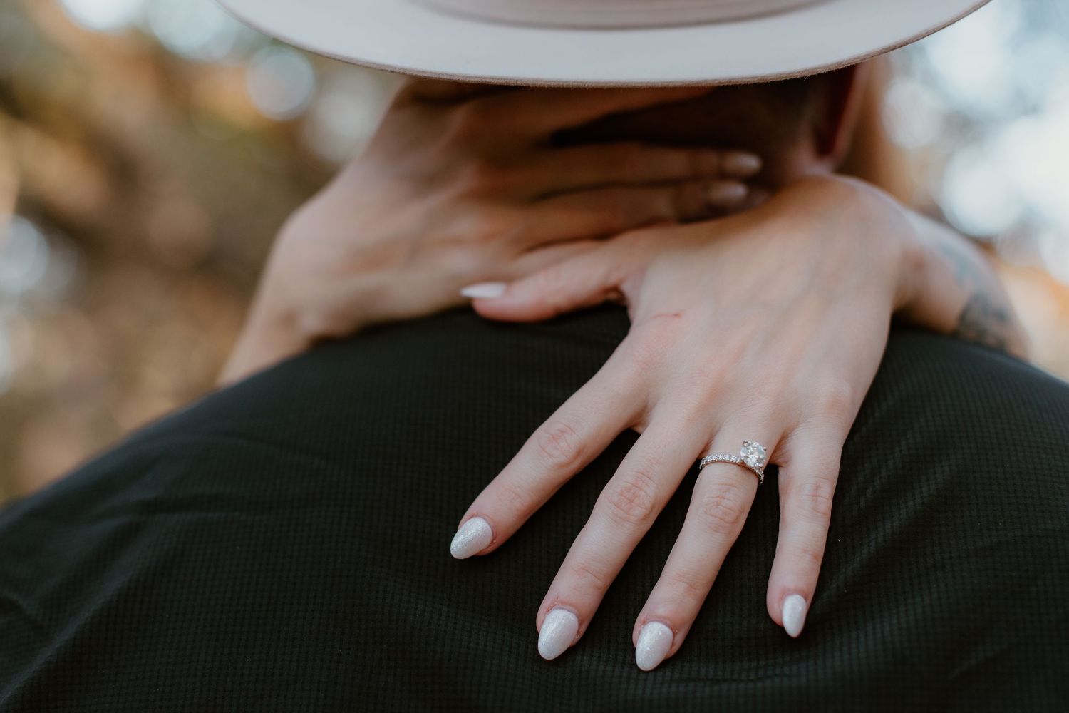 Close-up view of hands with white manicured nails resting on dark fabric.