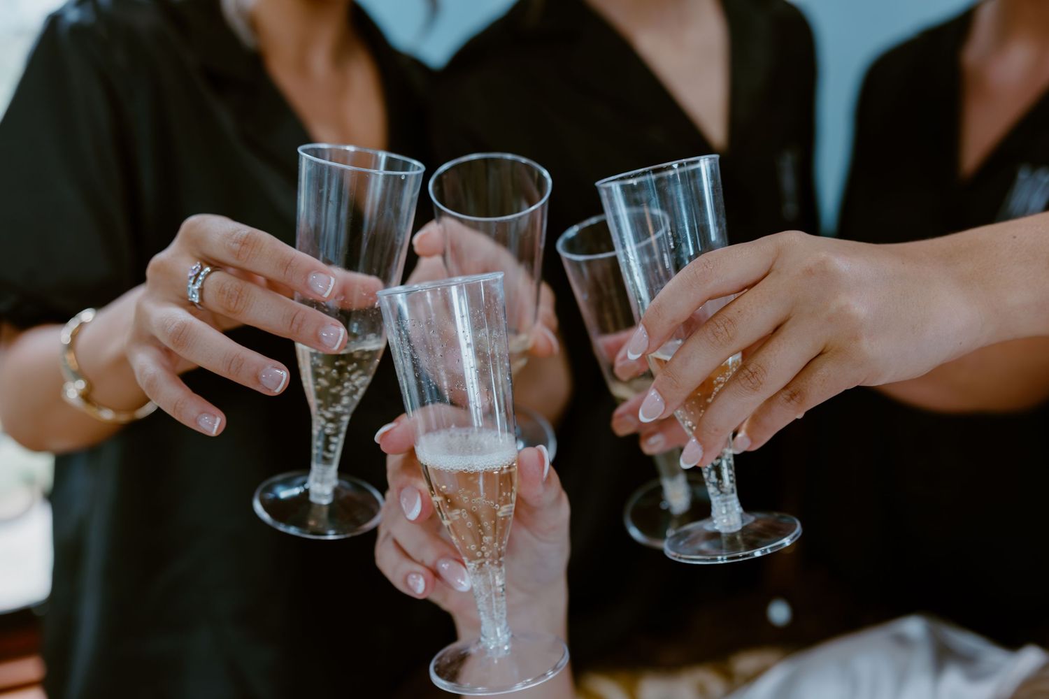 Group of women in black shirts clinking champagne flutes together in a celebratory toast.