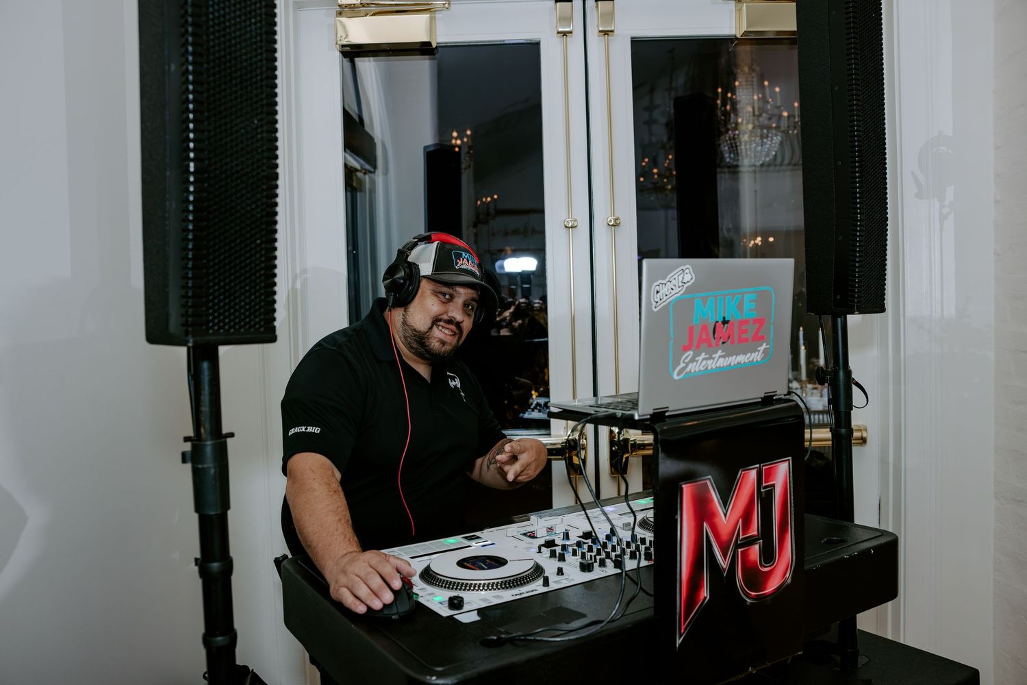 DJ wearing headphones mixes music at a turntable setup with a laptop and speakers at an elegant wedding reception.