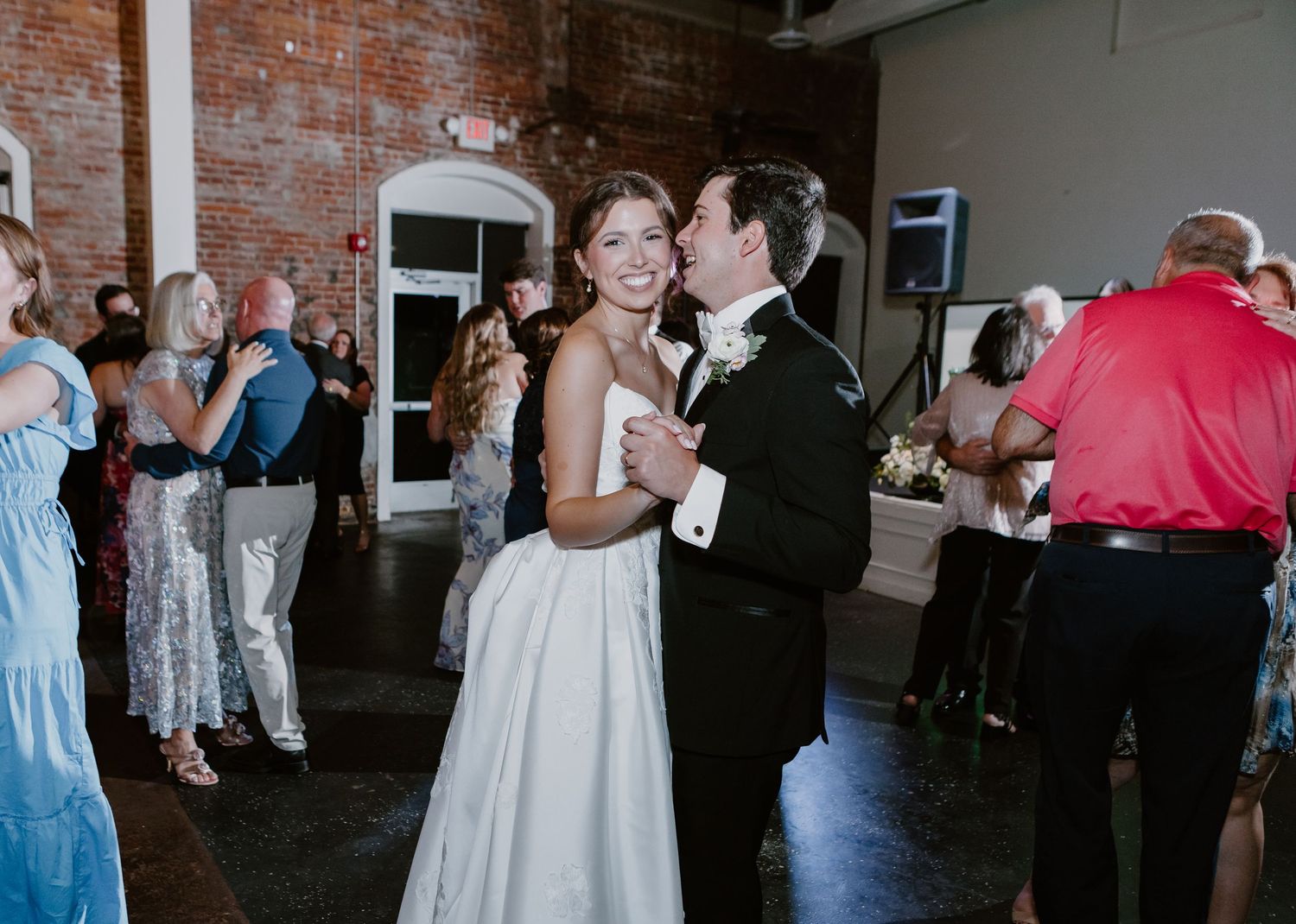 Bride and groom share a romantic first dance at their wedding reception in a rustic brick venue.