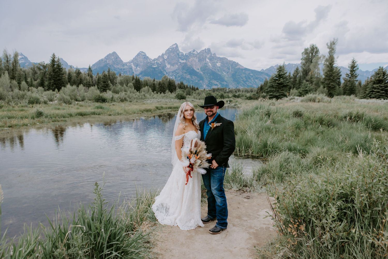Bride and groom posing by a river with Grand Teton mountains backdrop on their wedding day in Wyoming.