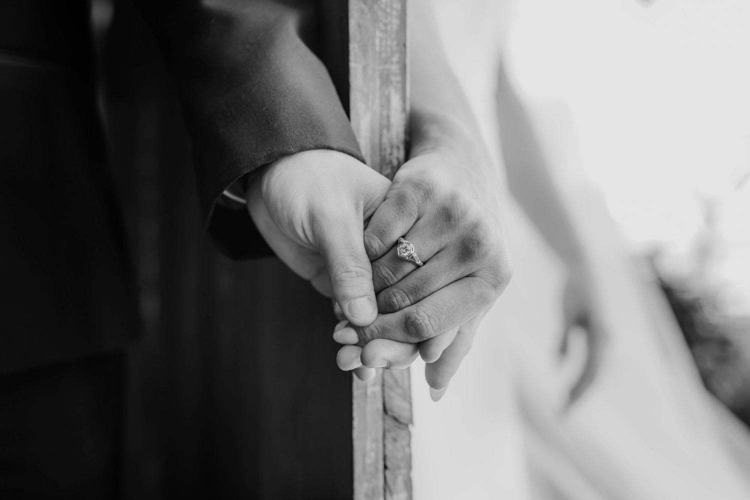 Black and white detail shot of couple holding hands through door frame.