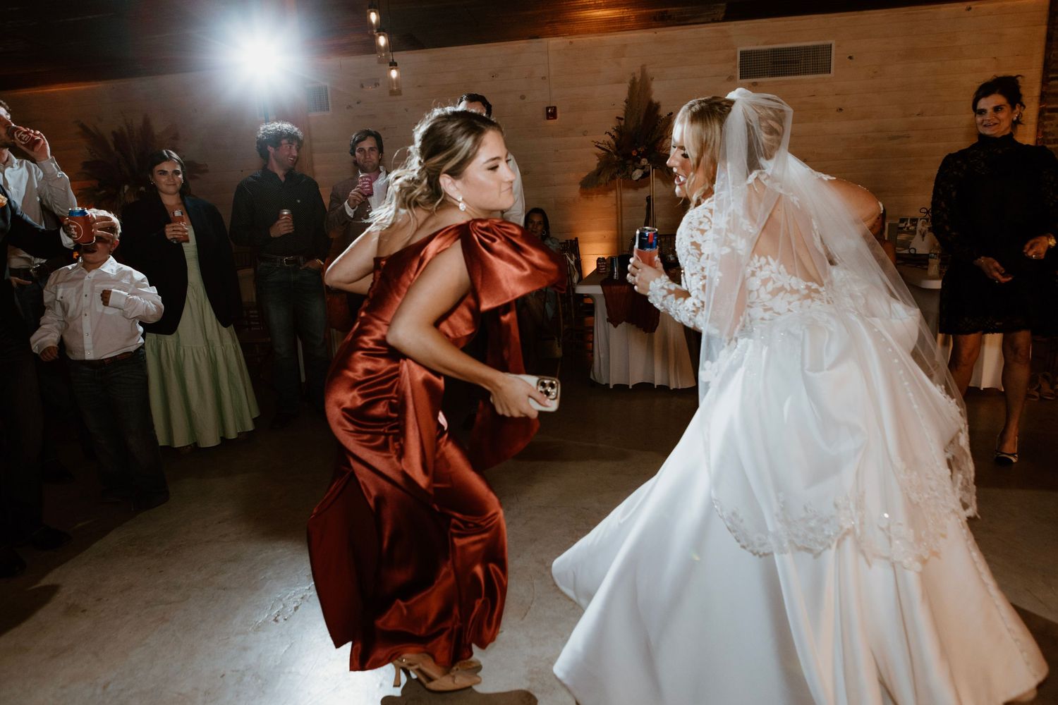 Bride in white gown dancing energetically with bridesmaid in red dress at wedding reception.