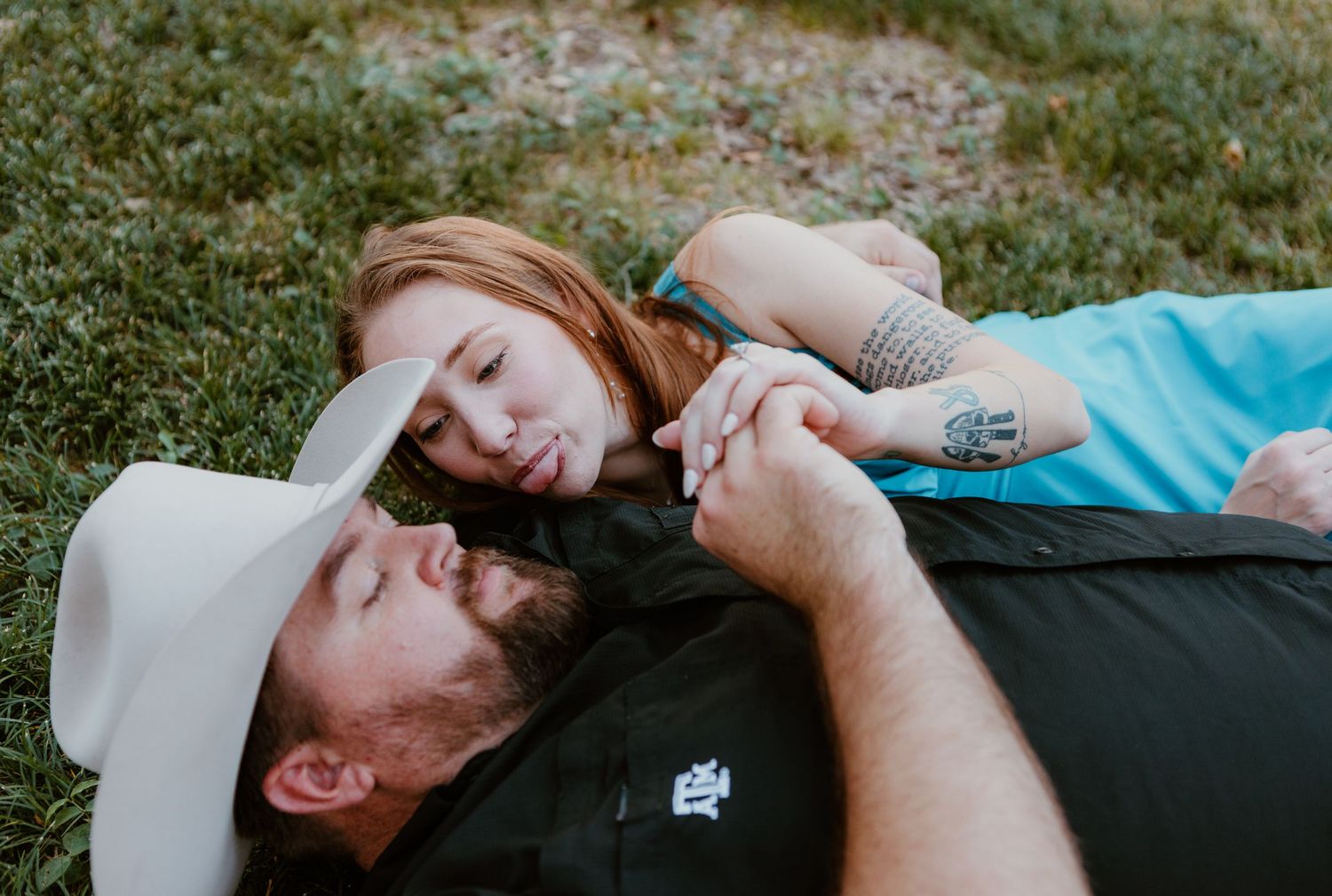 A person lies on green grass wearing a white baseball cap and turquoise shirt while relaxing outdoors.