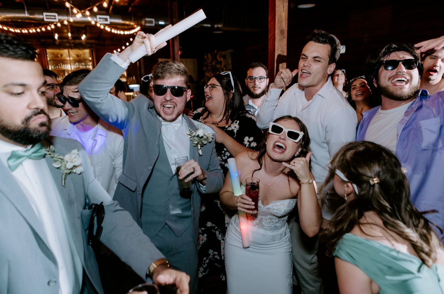 Wedding guests dancing and celebrating at a lively reception party wearing fun sunglasses.