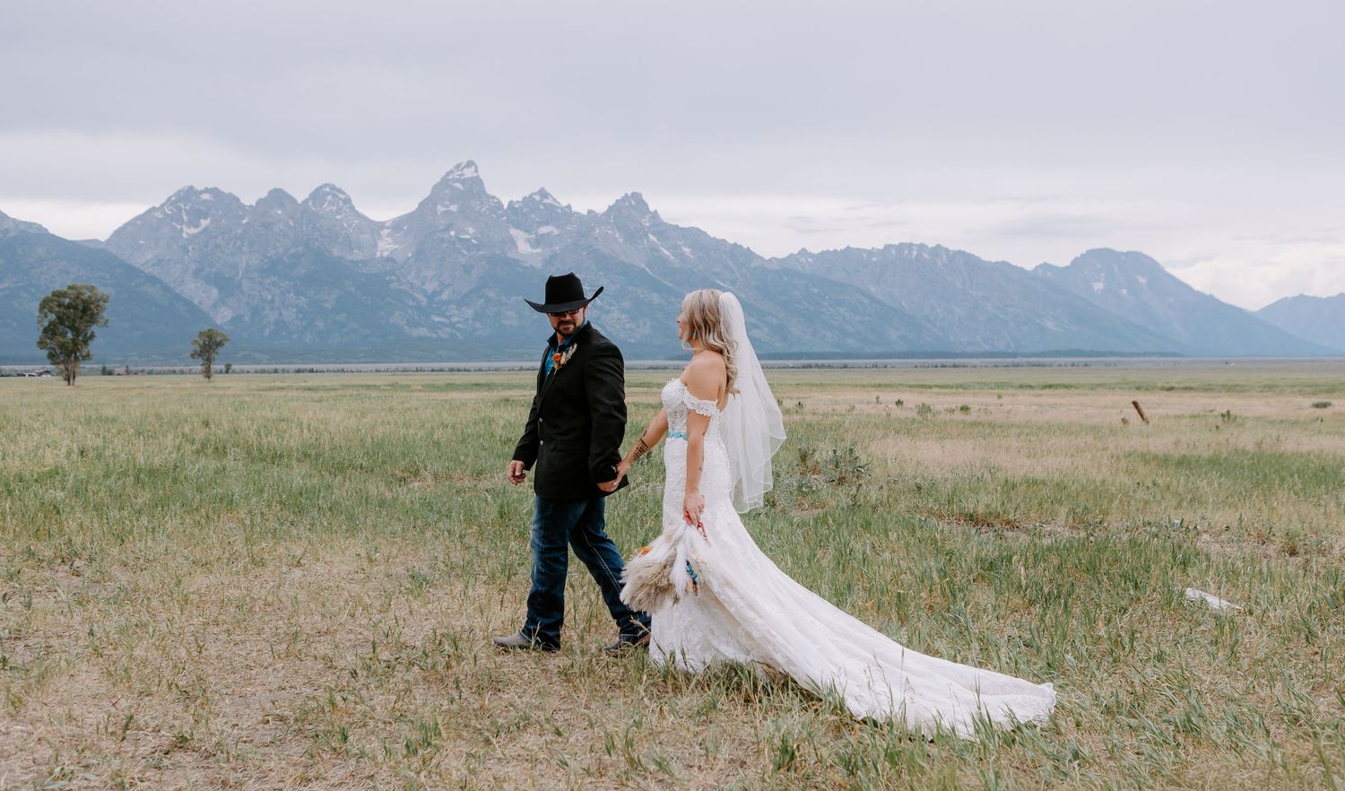 Bride and groom walking in a meadow with the Grand Teton mountains in the background on their wedding day.