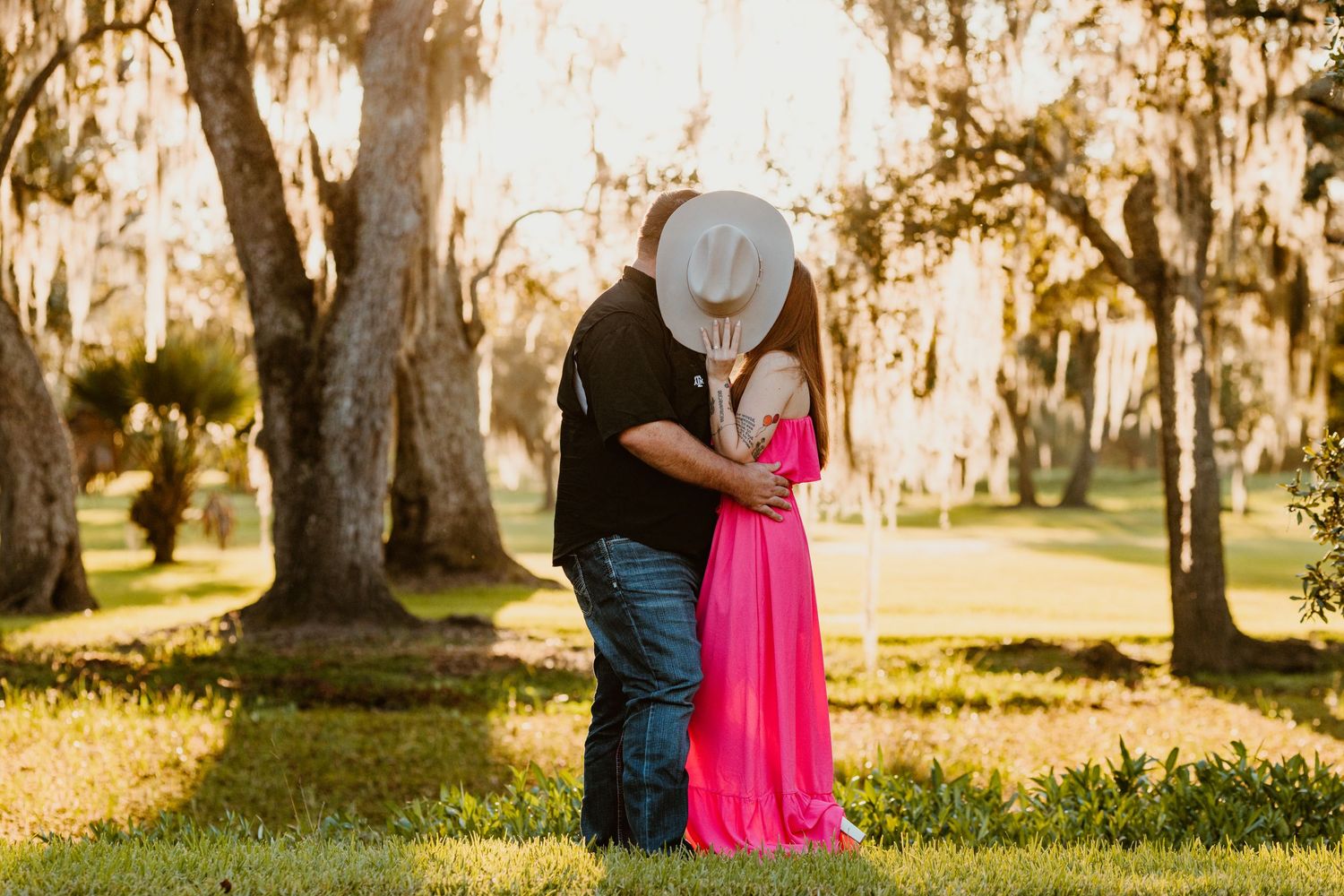 A couple embraces in a sun-drenched wooded area with Spanish moss hanging from the trees during a romantic photoshoot.