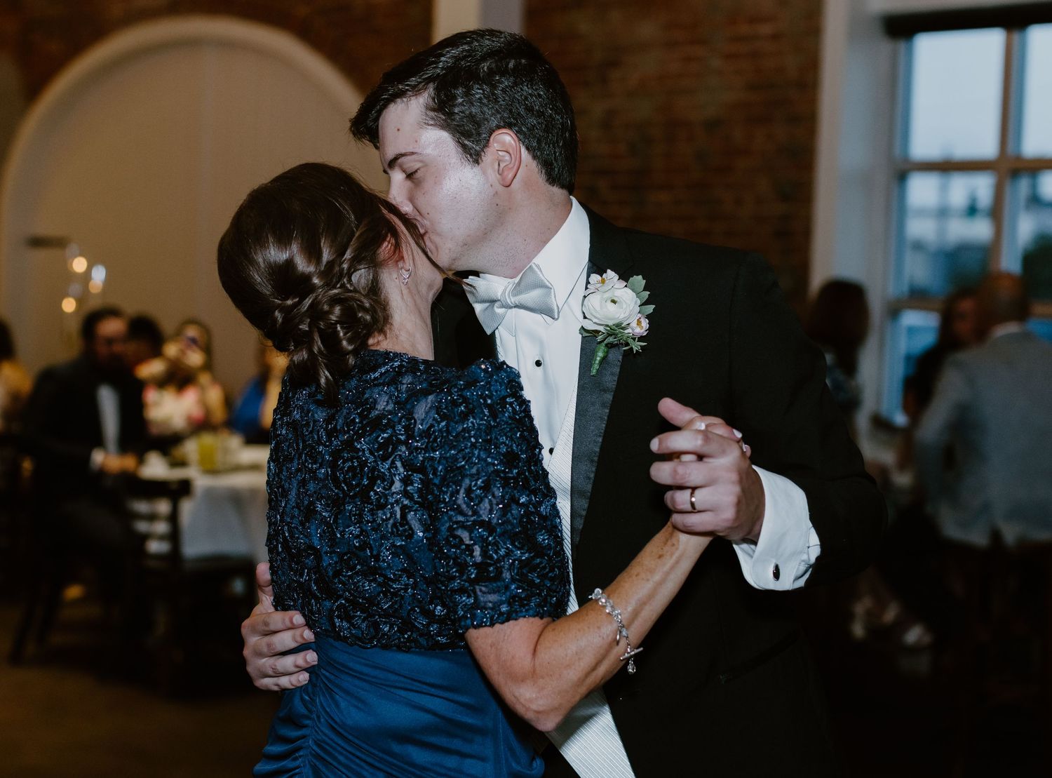 Groom shares a tender first dance kiss with his mother at a wedding reception.
