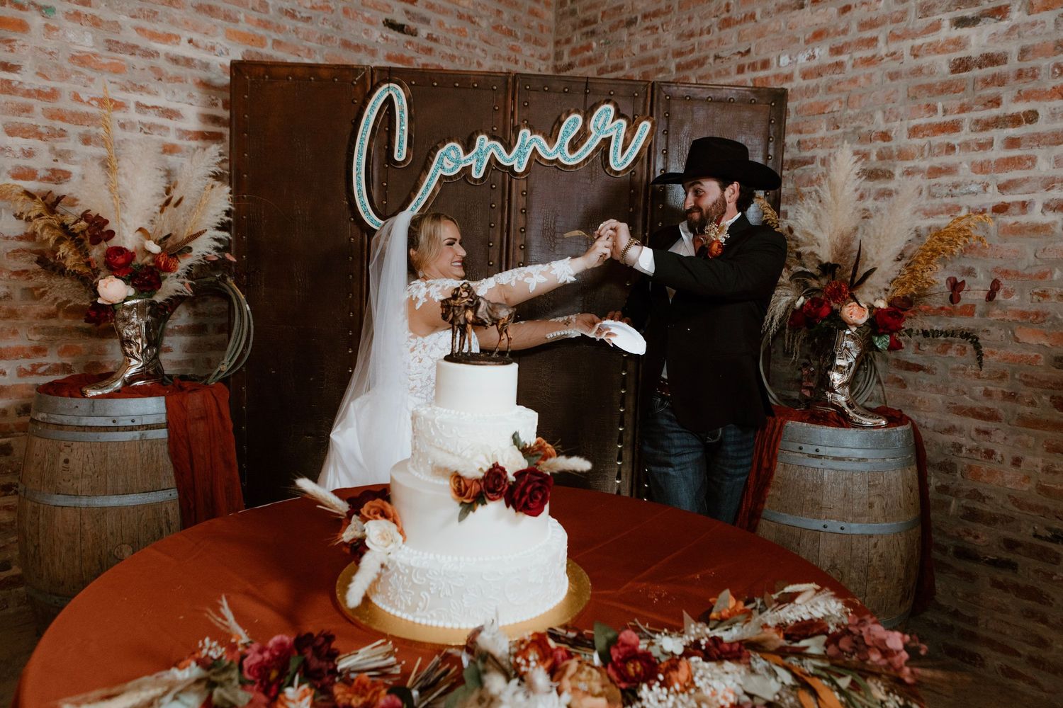 Bride and groom celebrate cake cutting at western-themed wedding with neon sign.