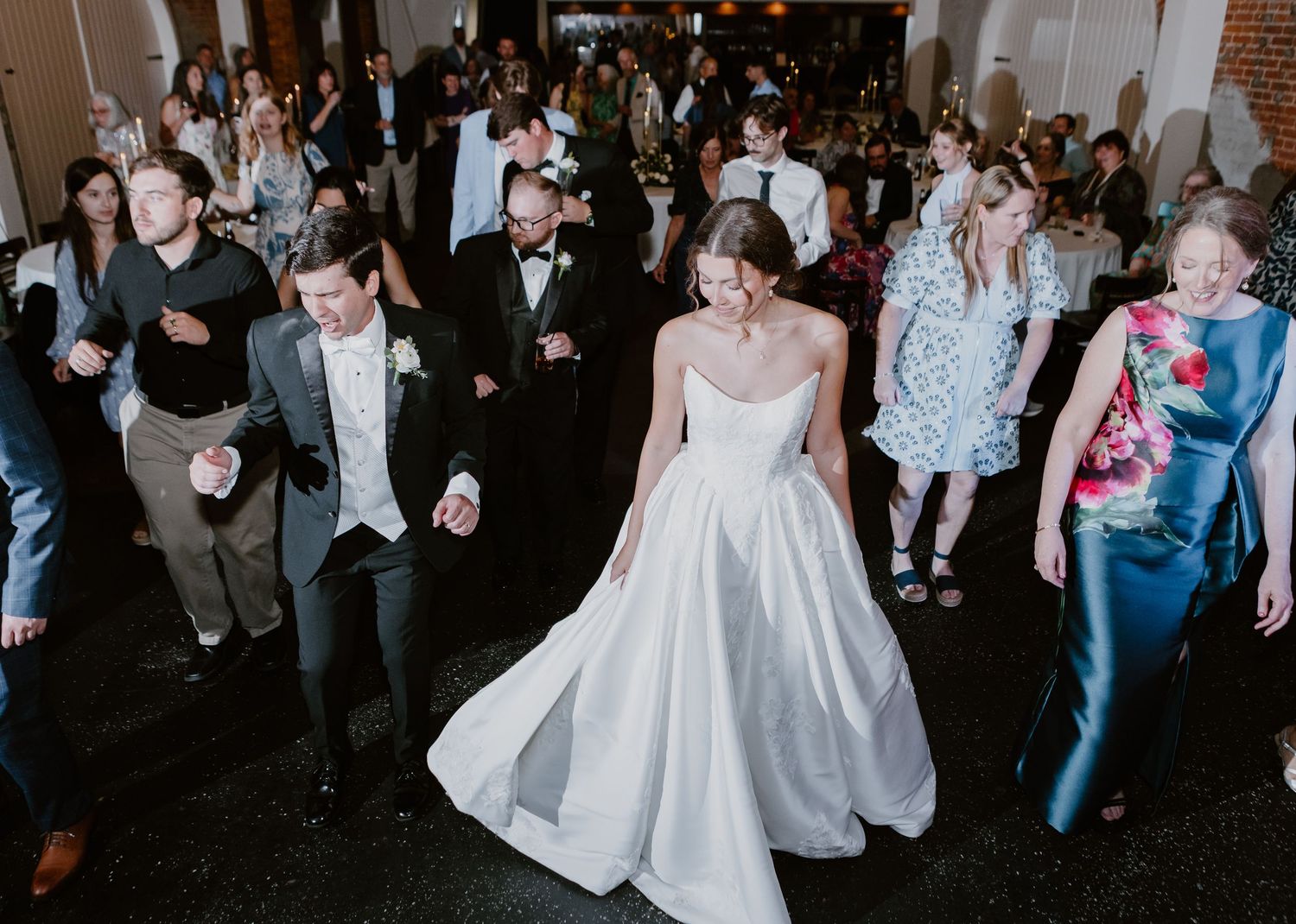 Bride in white ball gown dances with guests on wedding reception dance floor.