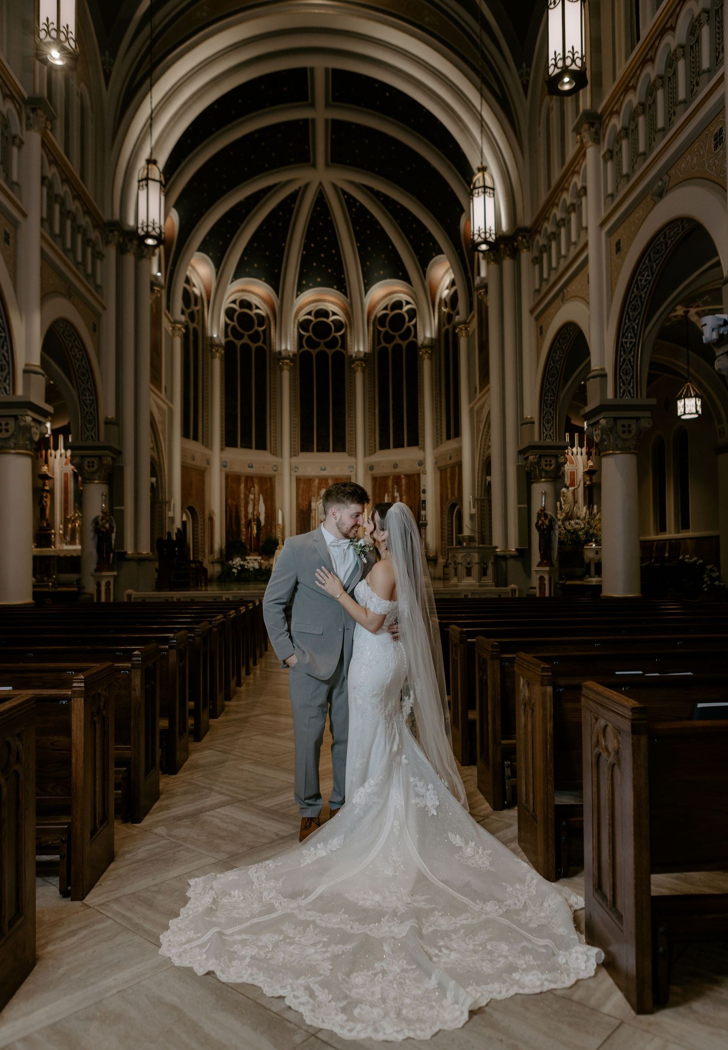 Bride and groom sharing romantic moment in stunning cathedral aisle with arched ceilings and pews.