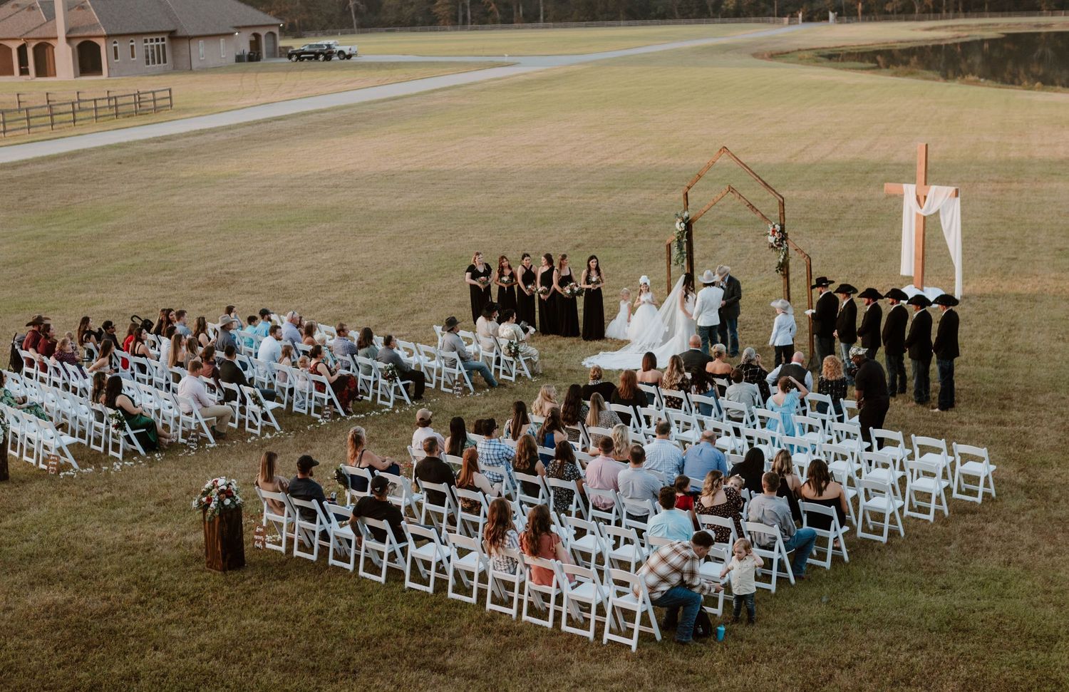Aerial view of an outdoor wedding ceremony setup with white chairs on a grassy field.