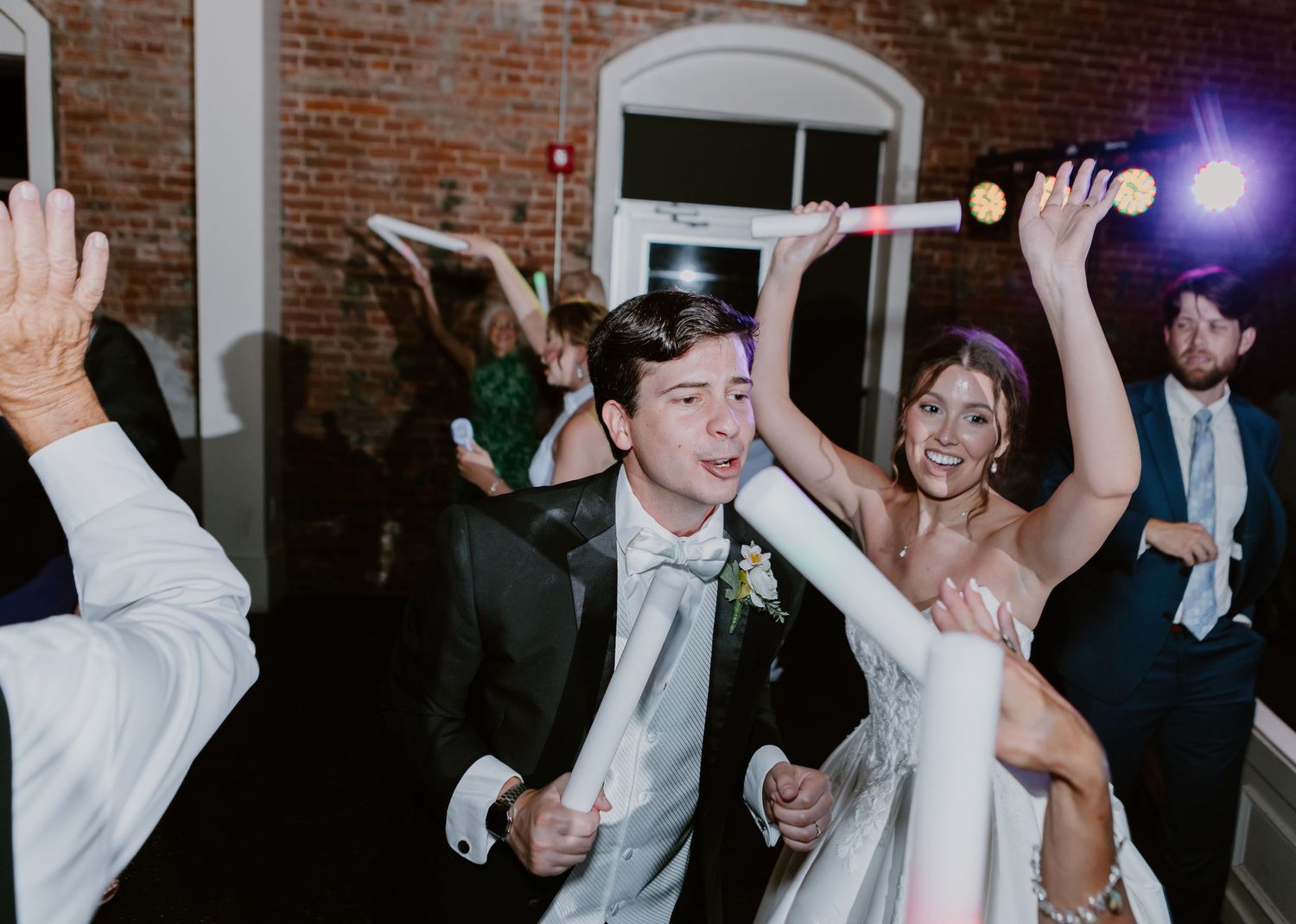 Bride and groom dancing joyfully at wedding reception with guests celebrating in background.