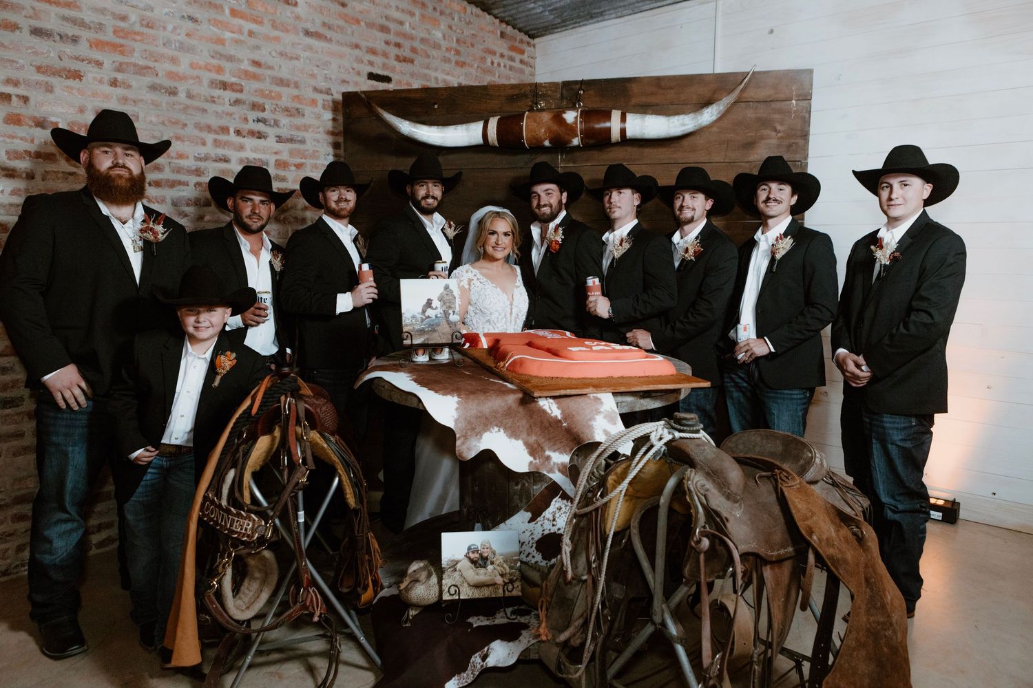 Wedding party in black suits and cowboy hats pose with longhorn decor.