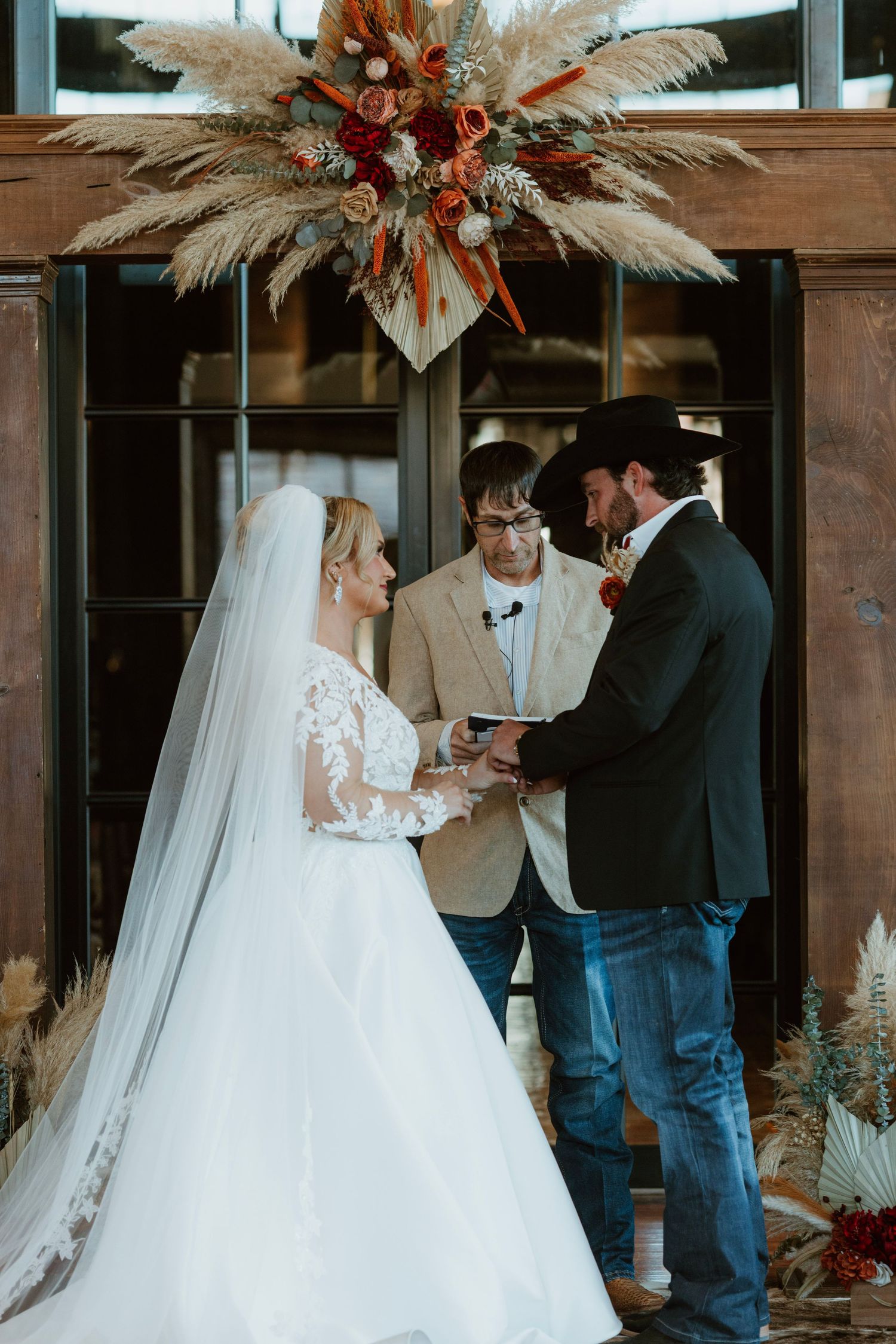 Bride and groom exchange vows at rustic wedding altar decorated with pampas grass and burnt orange floral arrangements.