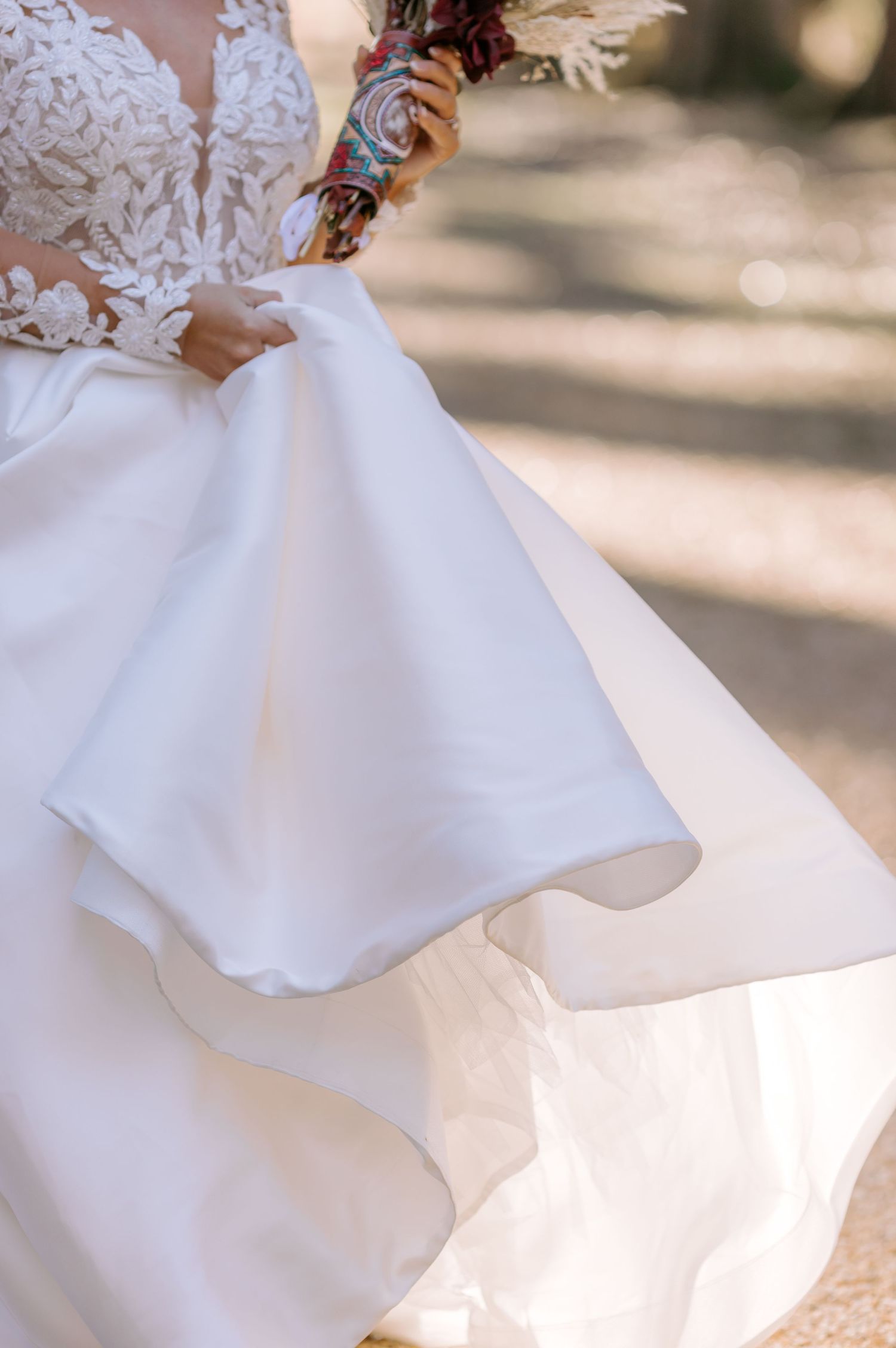 Close-up details of a flowing white wedding dress fabric with soft sunlit bokeh in the background.