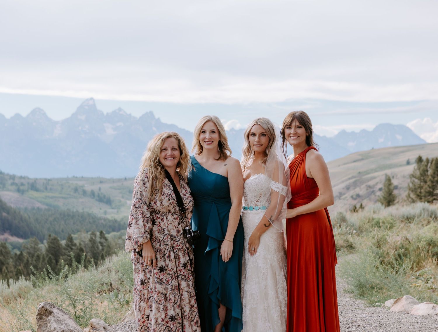 Four women posing outdoors at a mountain wedding with Grand Teton peaks in the background.