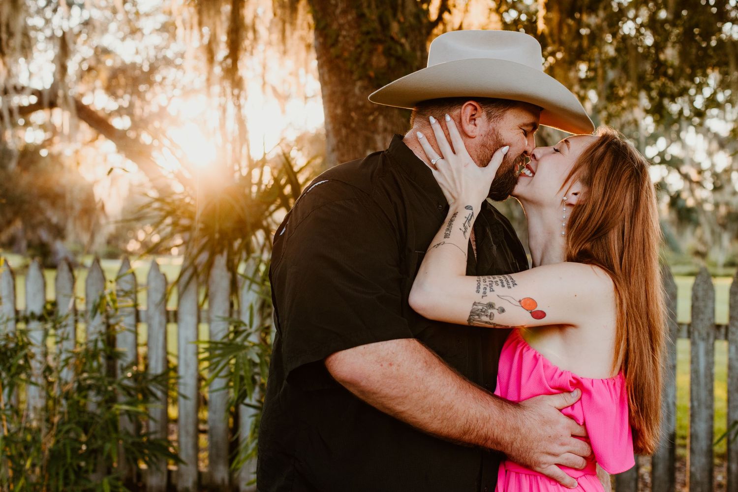 A romantic engagement photo series showing a couple embracing outdoors during golden hour with a rustic fence backdrop.
