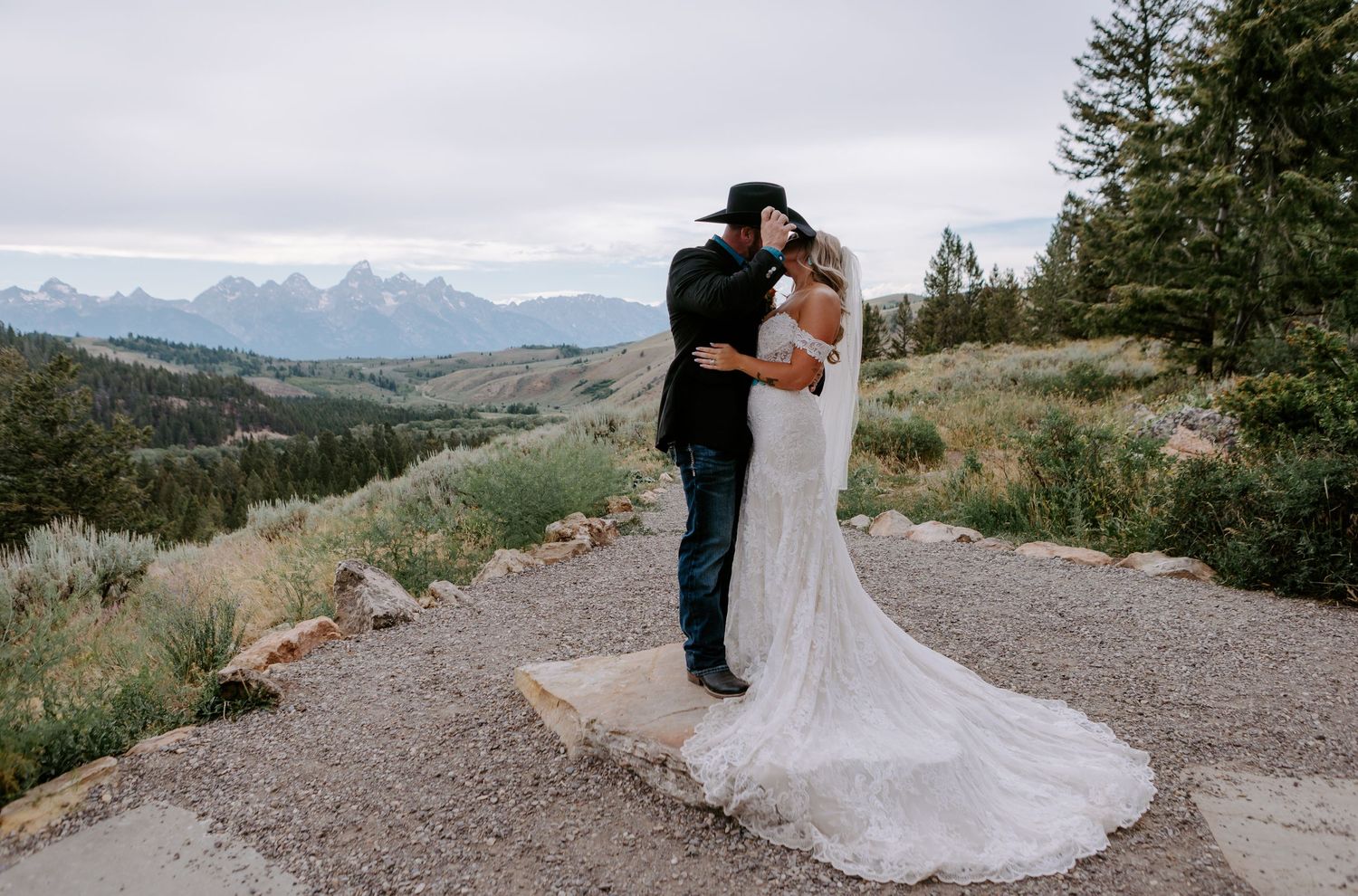 Bride and groom share a kiss on a scenic mountain overlook with Grand Teton peaks in the background.