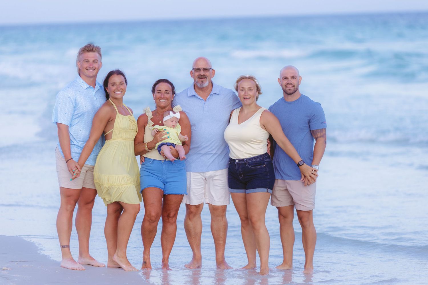 A group of people standing together on a beach at sunset with ocean waves in the background.