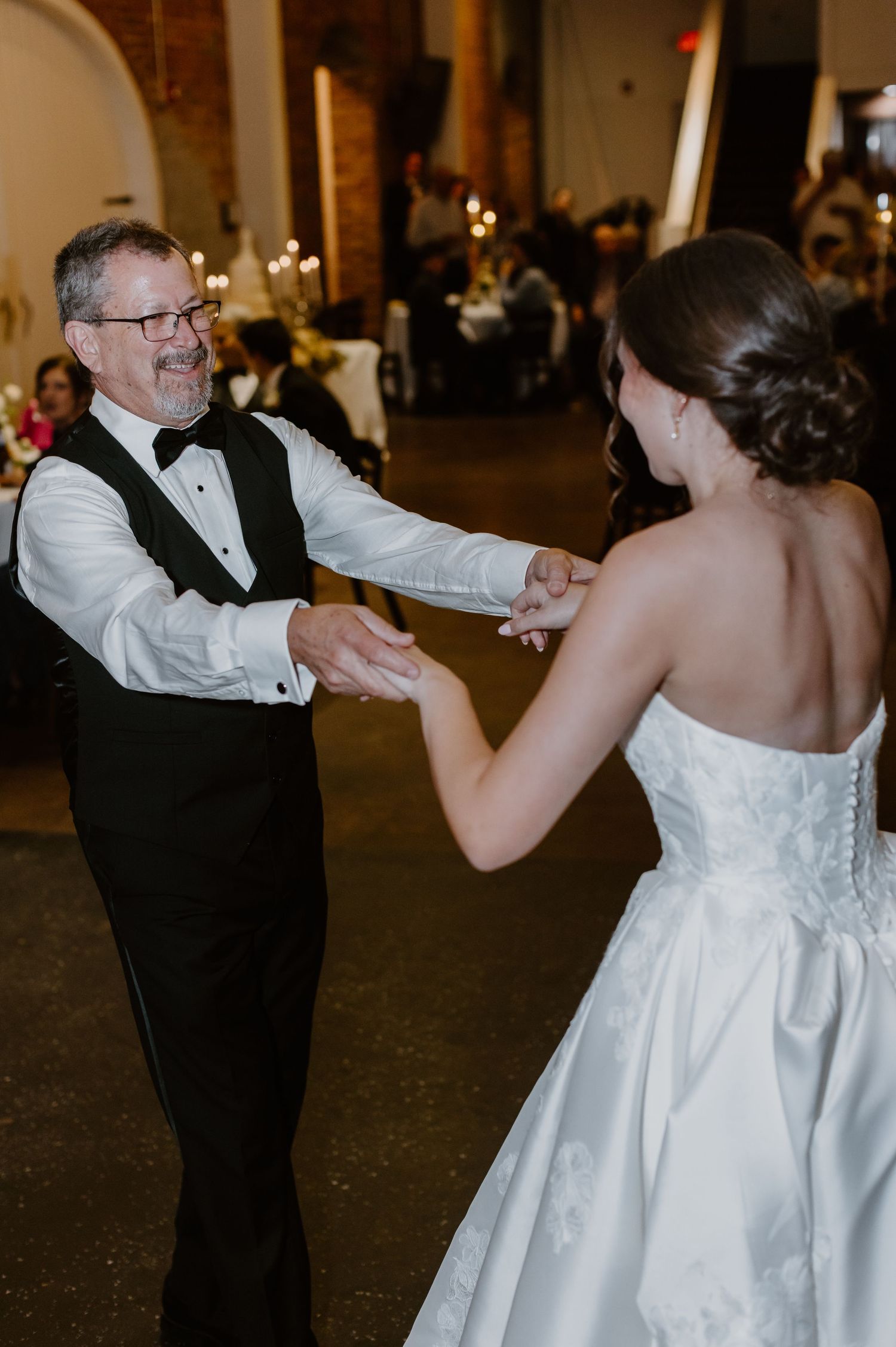 Father and bride hold hands during emotional father-daughter dance at wedding reception.