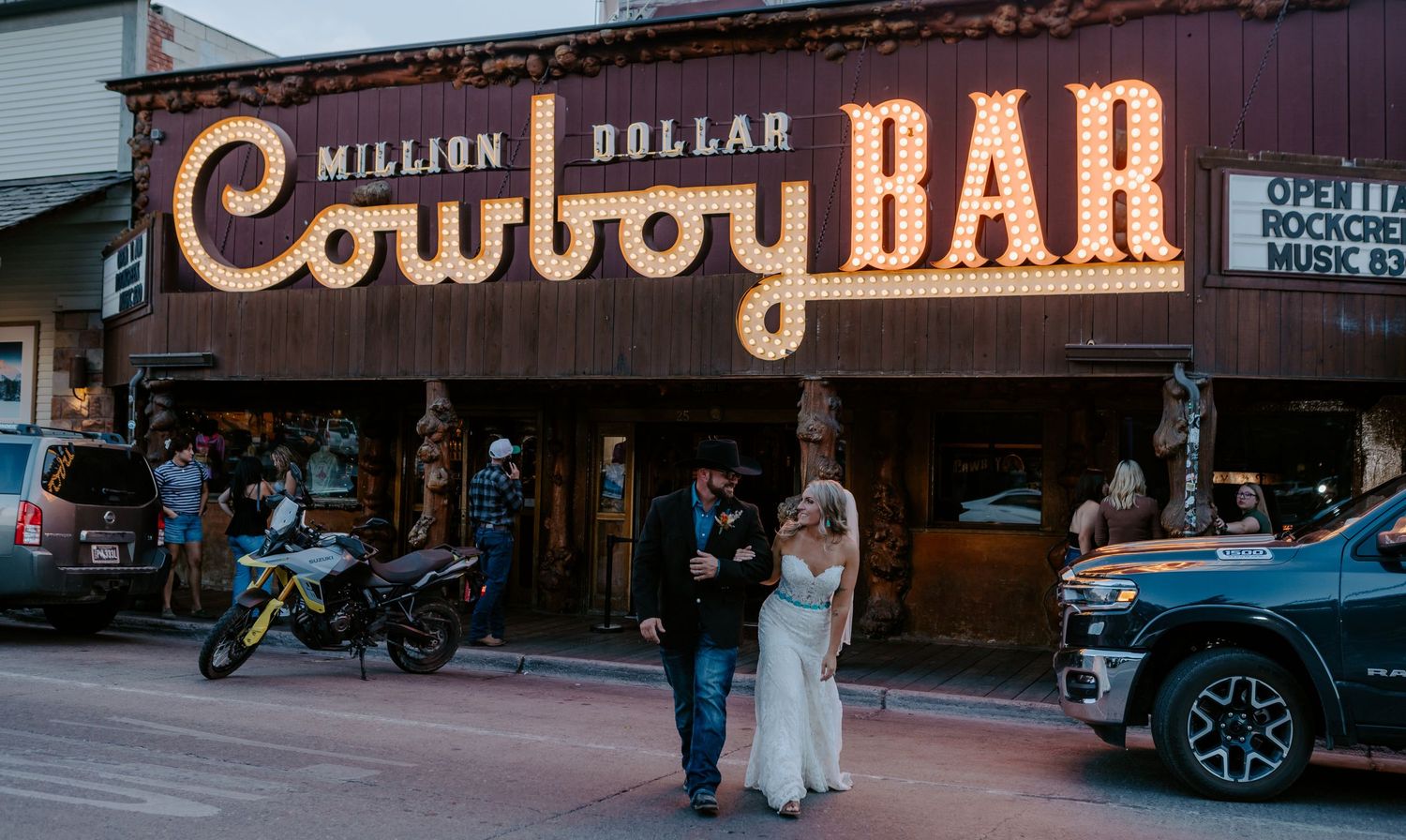 Couple in wedding attire poses in front of the iconic Million Dollar Cowboy Bar sign in Jackson Hole, WY.
