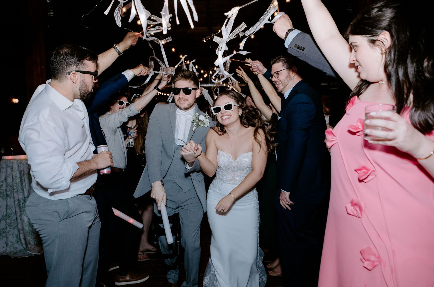 Bride and groom exit through streamer tunnel surrounded by cheering wedding guests.